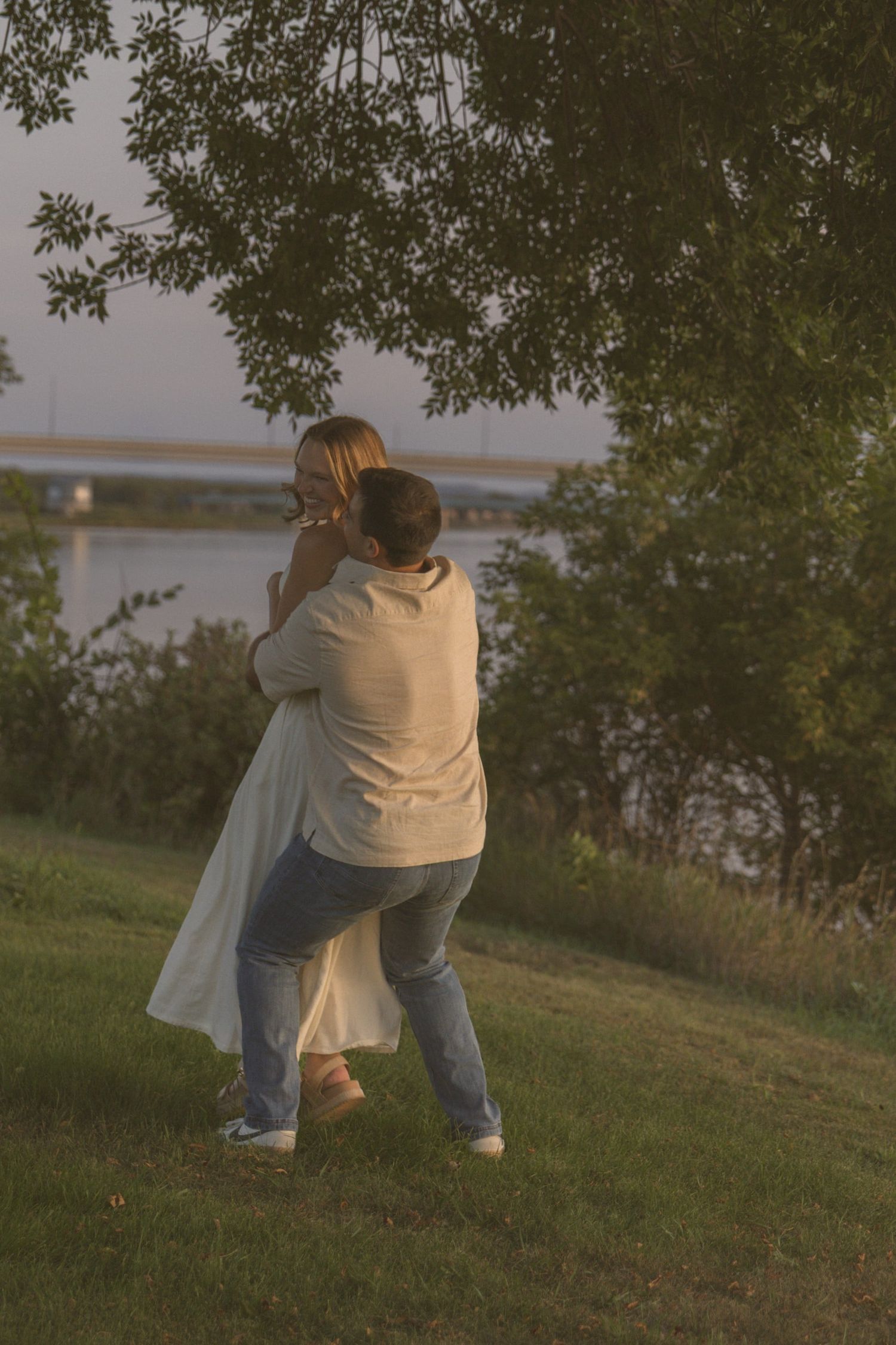 A couple dances and spins together on a grassy slope with a lake in the background.