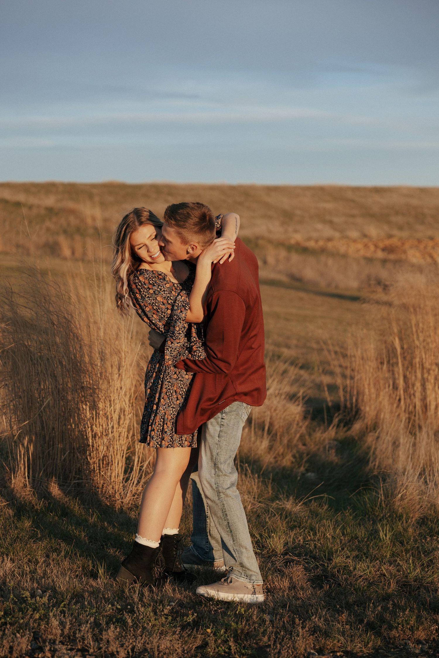 Couple sharing an intimate moment in golden sunlight among tall prairie grass.