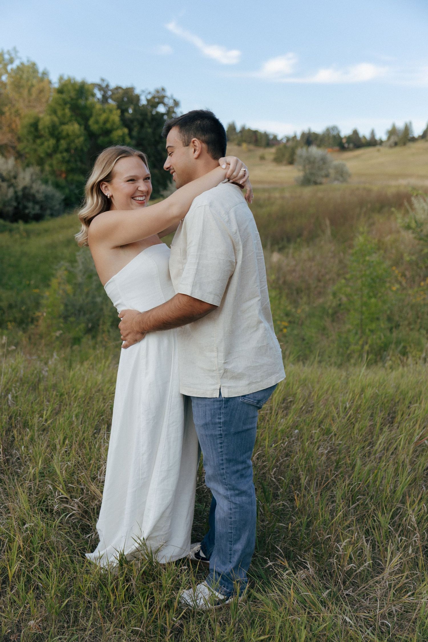 A couple shares an intimate embrace in a sunlit meadow during their photoshoot.