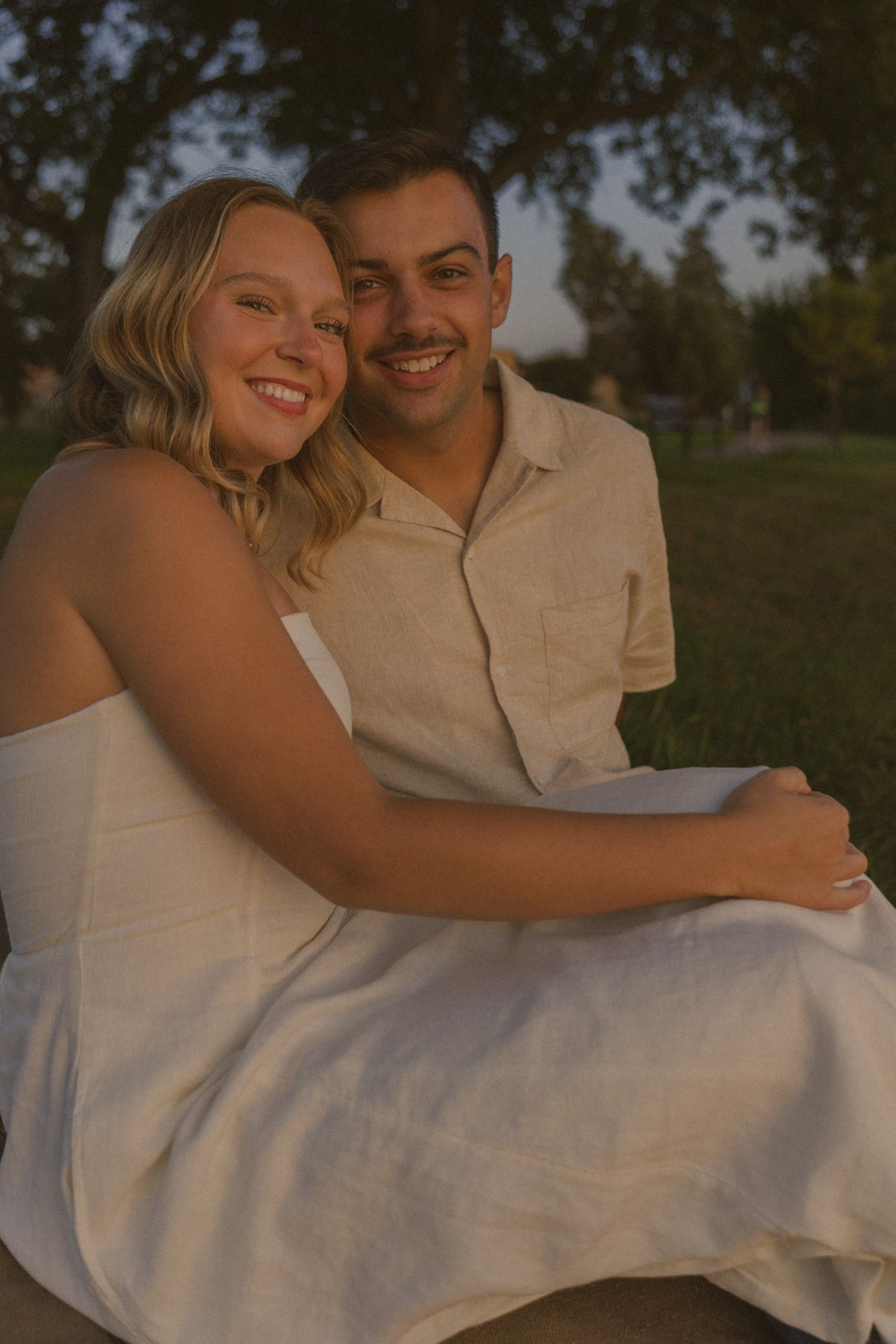 A joyful couple embraces and laughs together during a sunset photoshoot by a lake.