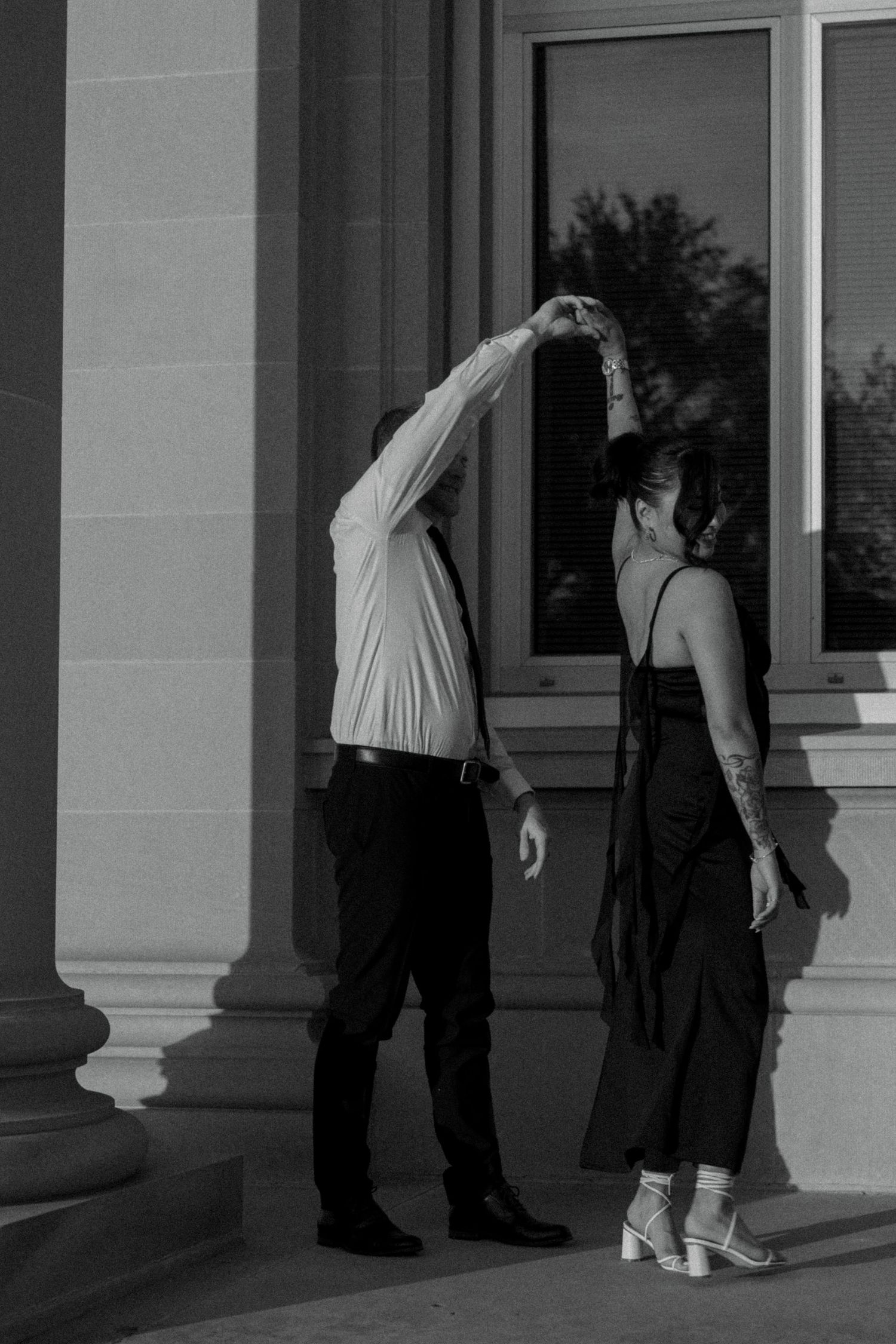 A couple shares tender moments in the shadows of a building's columned entrance.