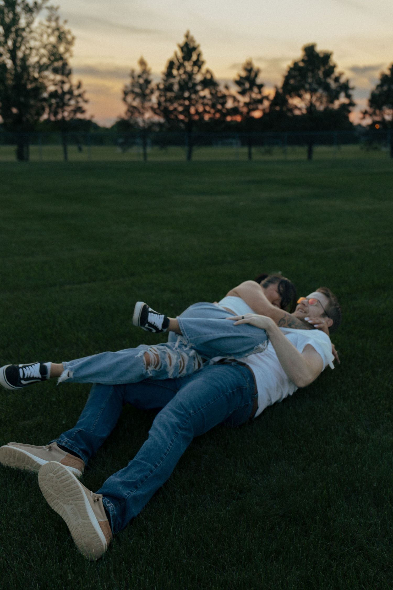 Two people lying on grass during golden hour with dramatic lighting.