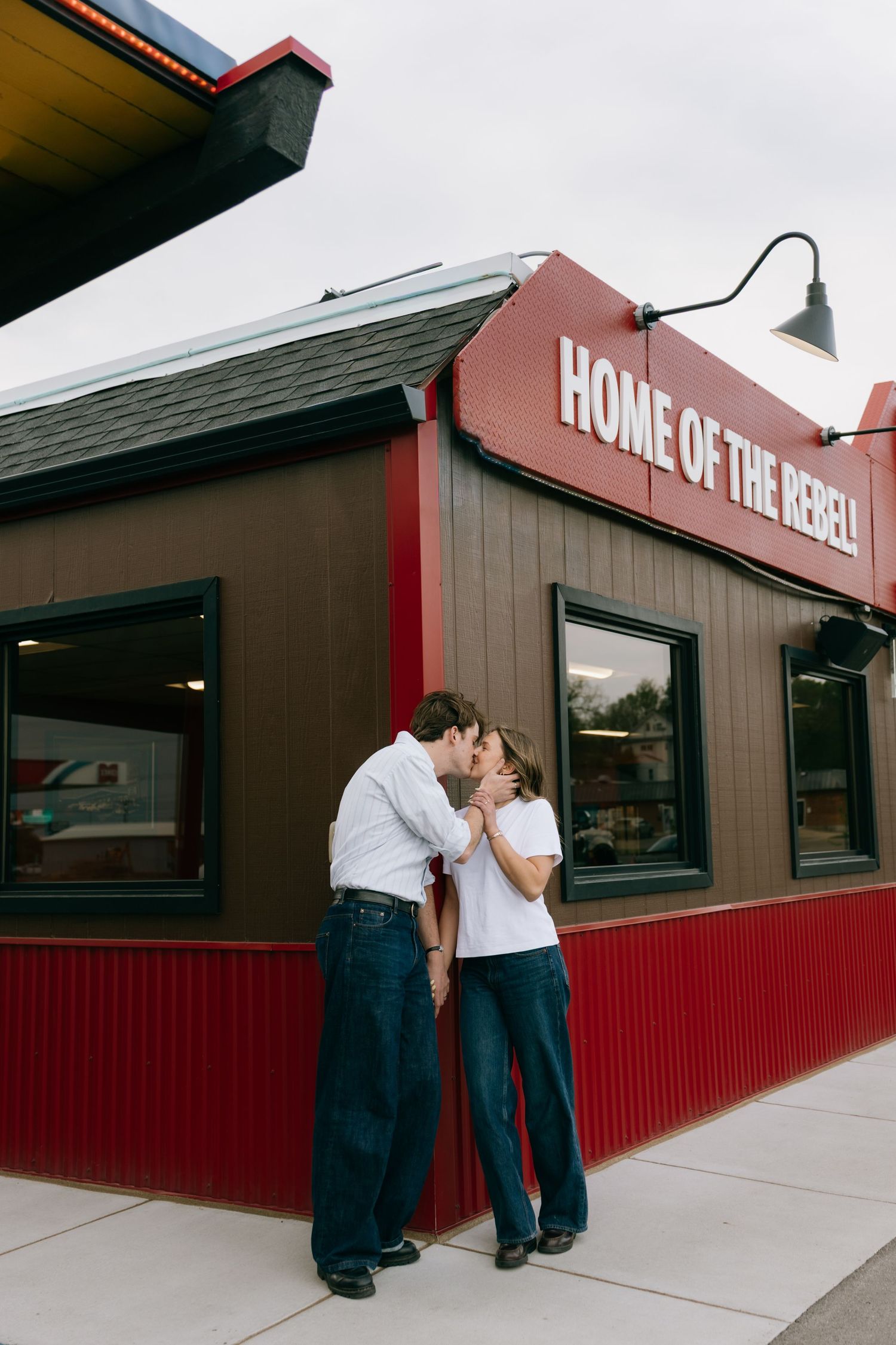 Couple sharing a romantic kiss outside a diner with Home of the Rebel sign.