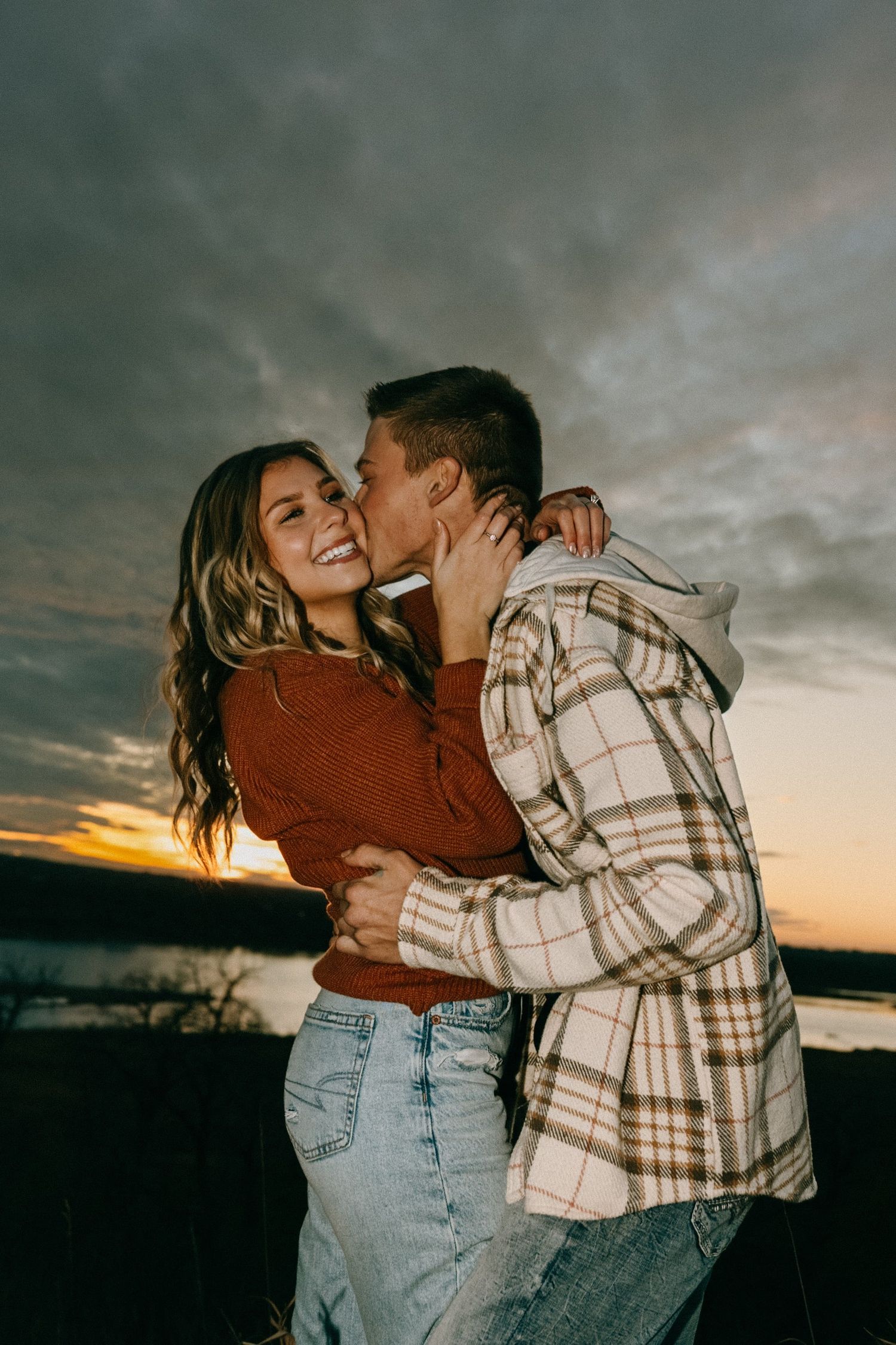 Candid moment of a couple laughing and embracing against a moody sunset sky.