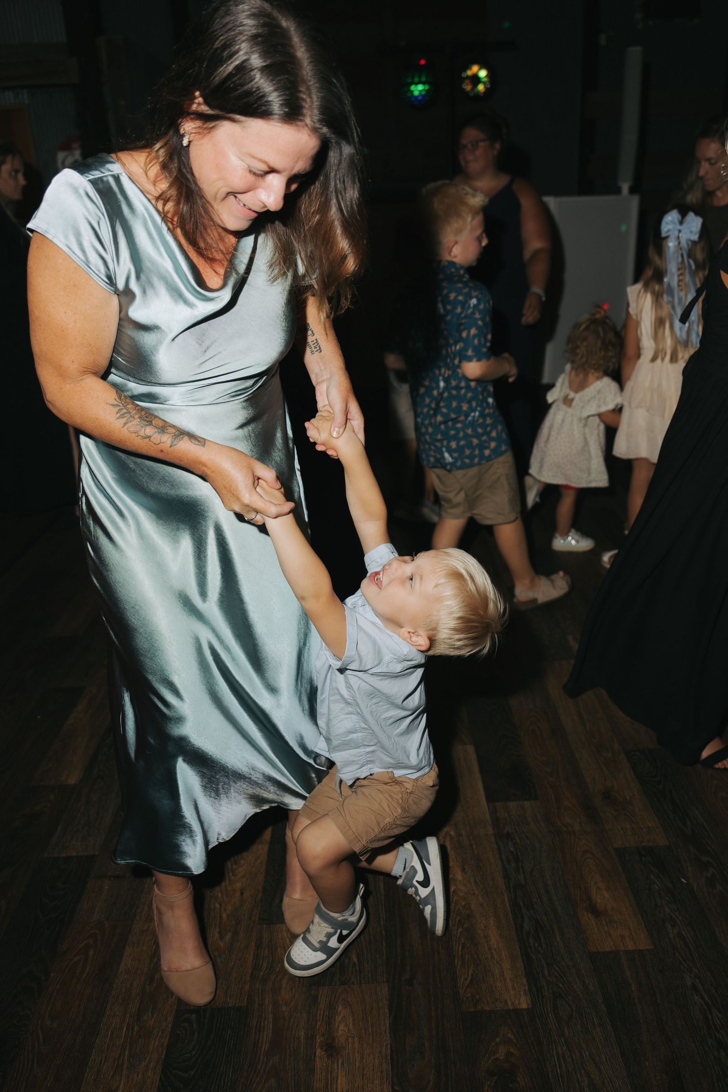 Woman in satin dress dancing with a toddler boy at a wedding reception on a dark dance floor.