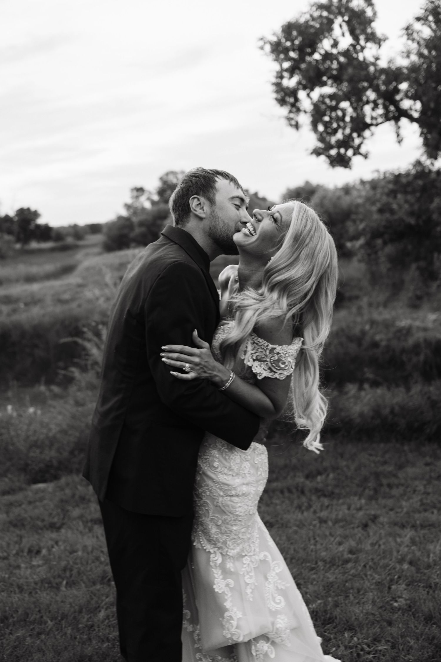 Black and white photo of bride and groom sharing a romantic kiss in a lush outdoor setting.