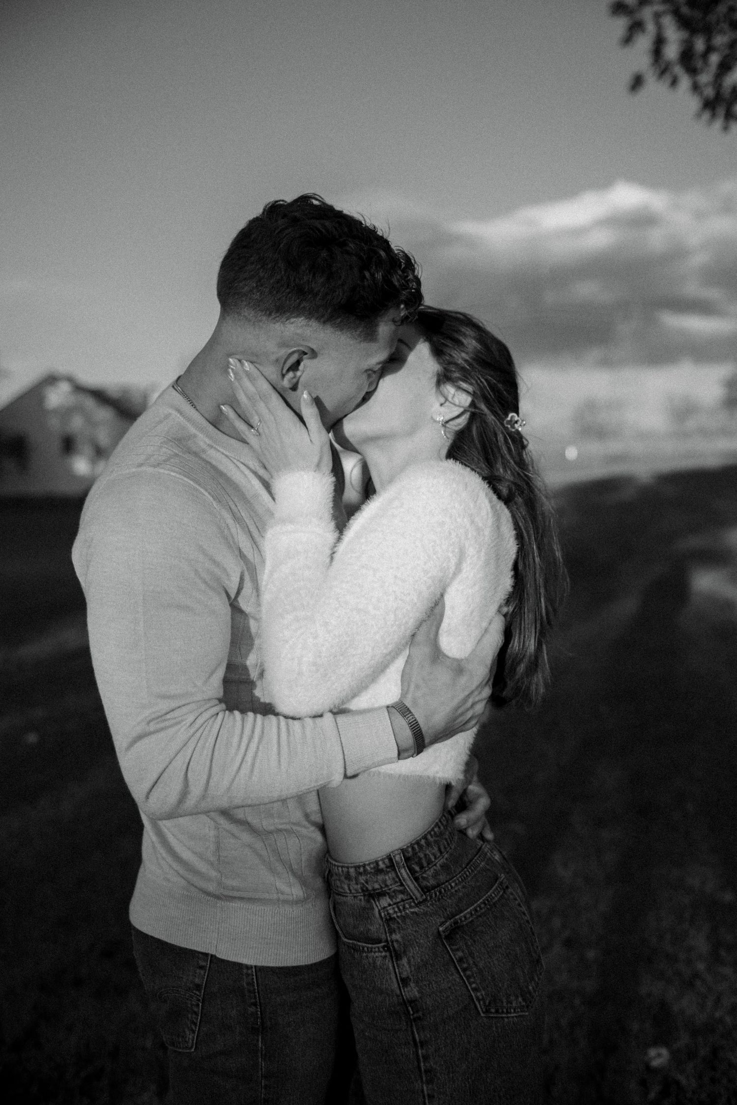 Black and white photo series showing a romantic couple embracing and kissing in a field at sunset.