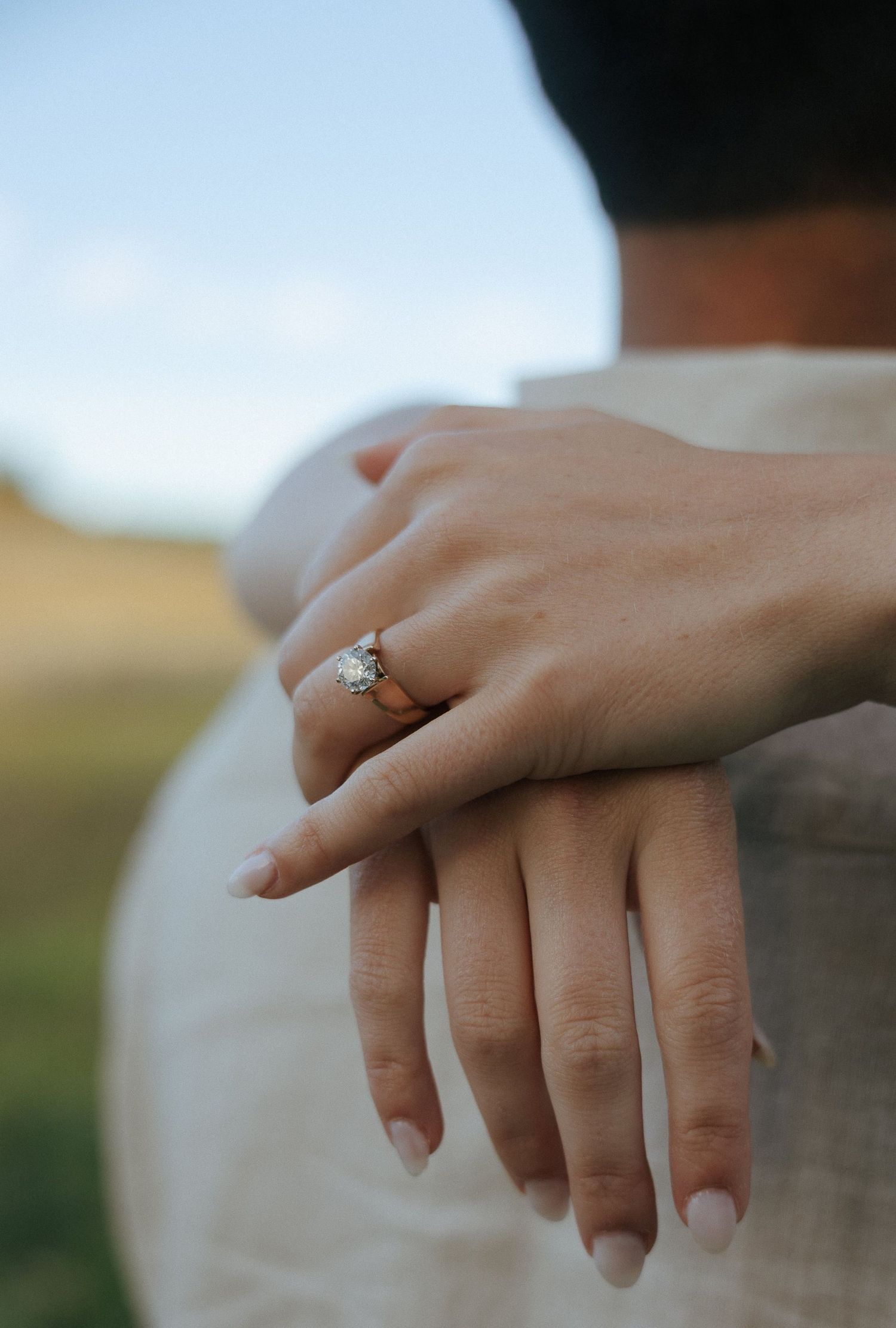 Close-up of an engagement ring on a woman's hand with a blurred natural background.