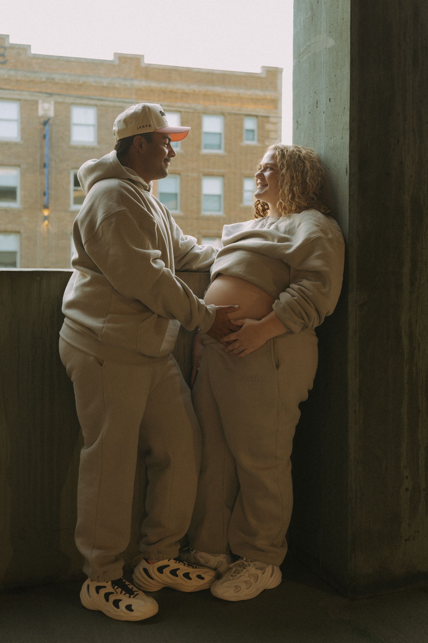 couple smiling looking at each other while holding baby bump for maternity session downtown Bismarck
