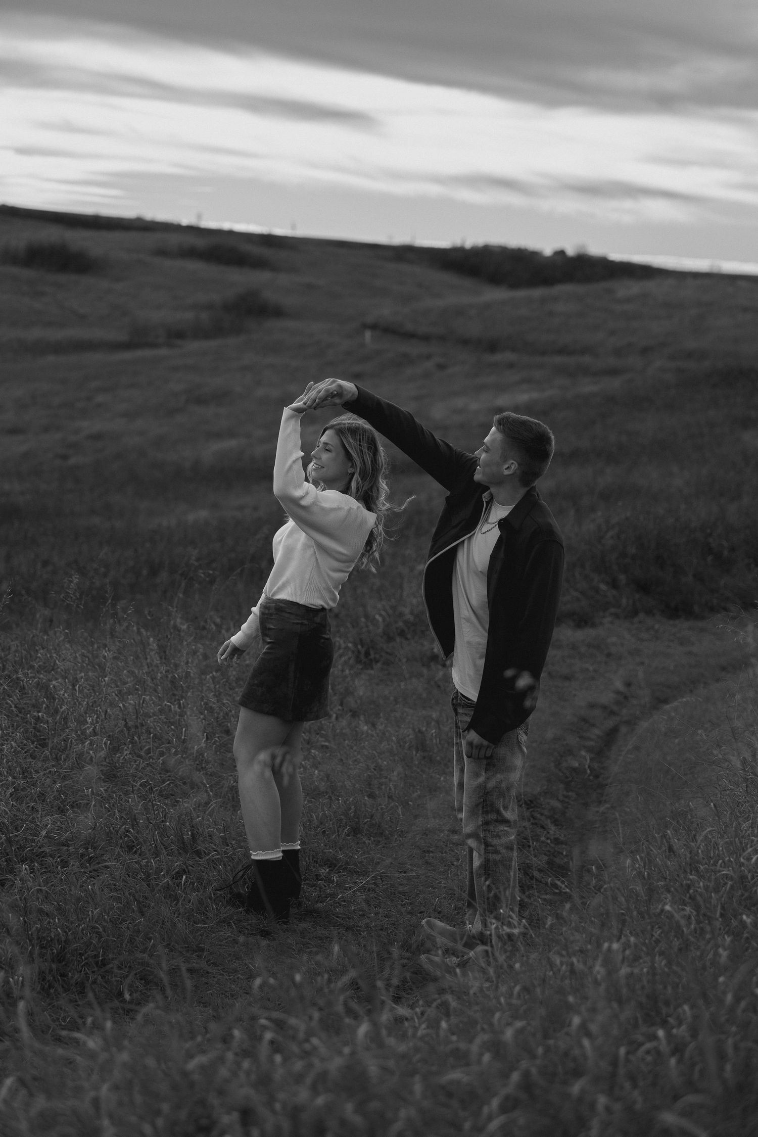 Playful couple stretches in a field of tall grass at dusk.