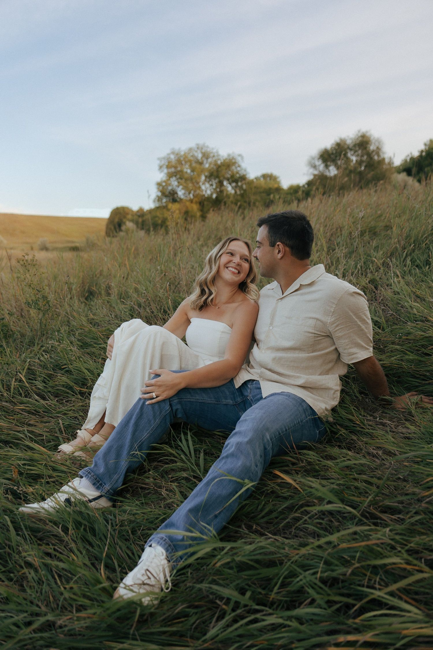 A couple lounges together in tall grass during a romantic outdoor photoshoot.