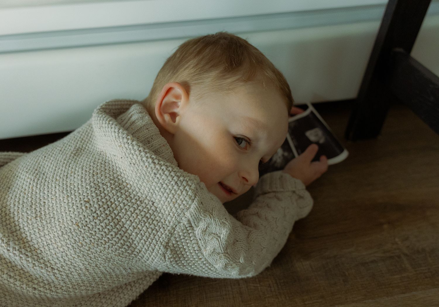 toddler holding ultrasound photos giggling hiding from camera
