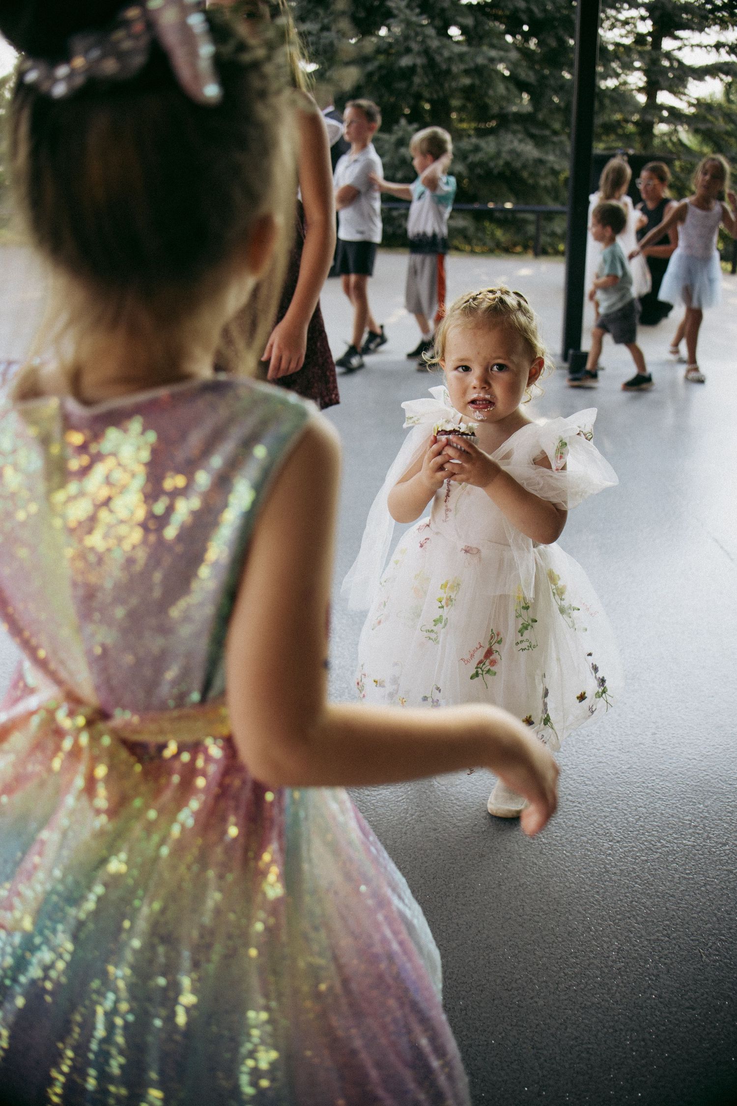 Two young girls in fancy dresses dance together at an outdoor children's party celebration.