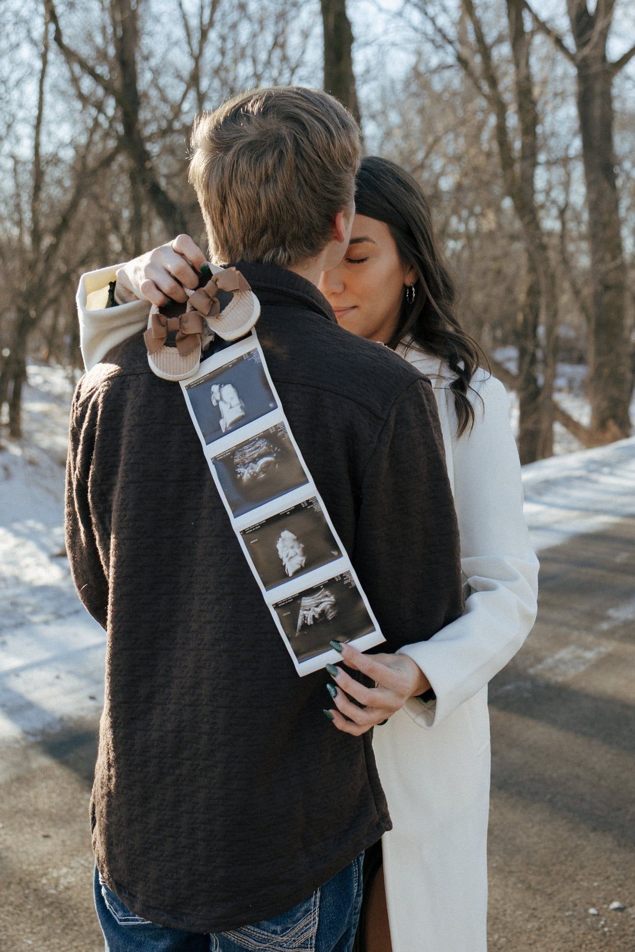 Couple kissing in snowy trees in Bismarck with ultrasound photos