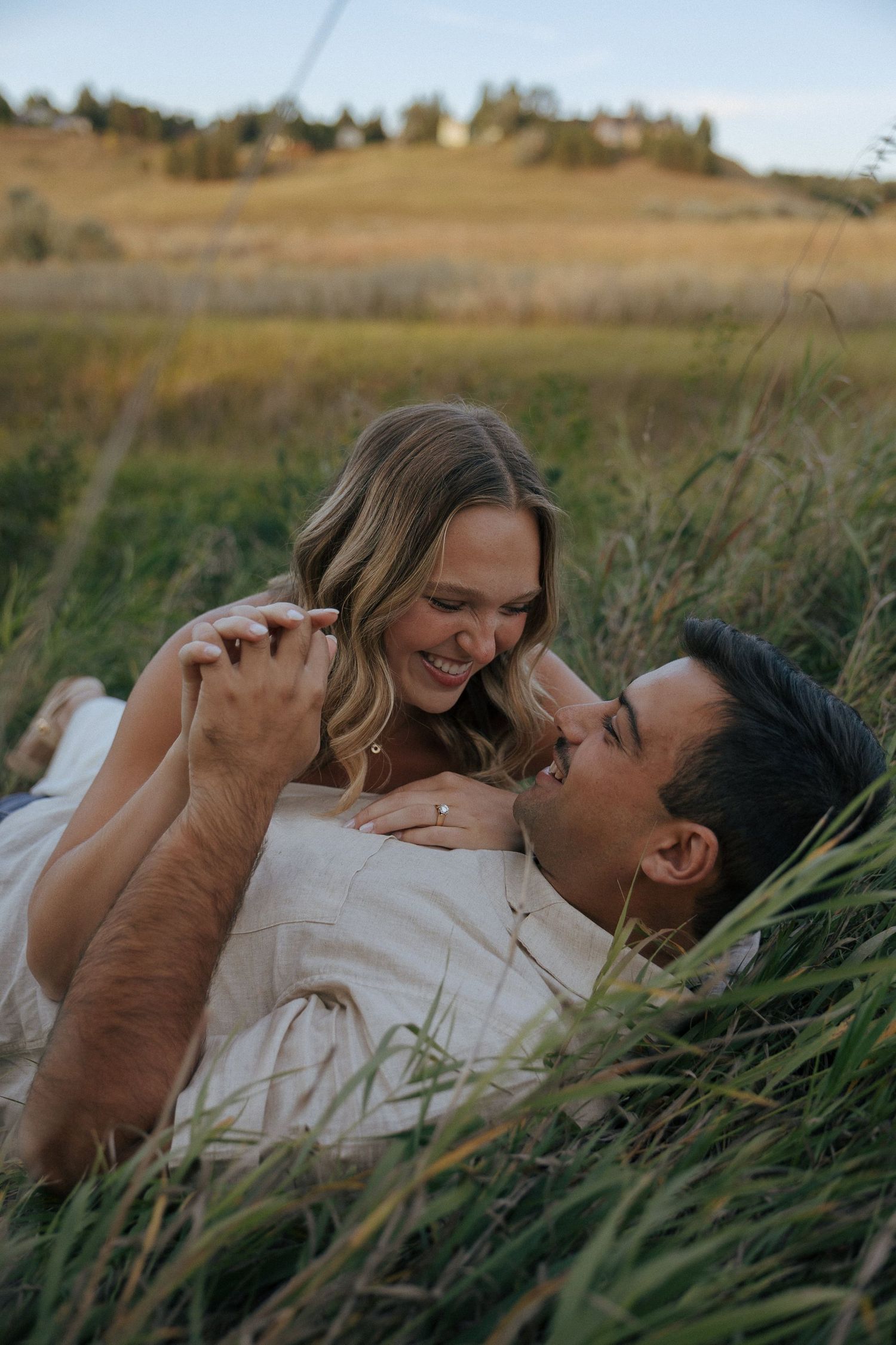 Two people share playful laughter while relaxing in a meadow of tall grass.