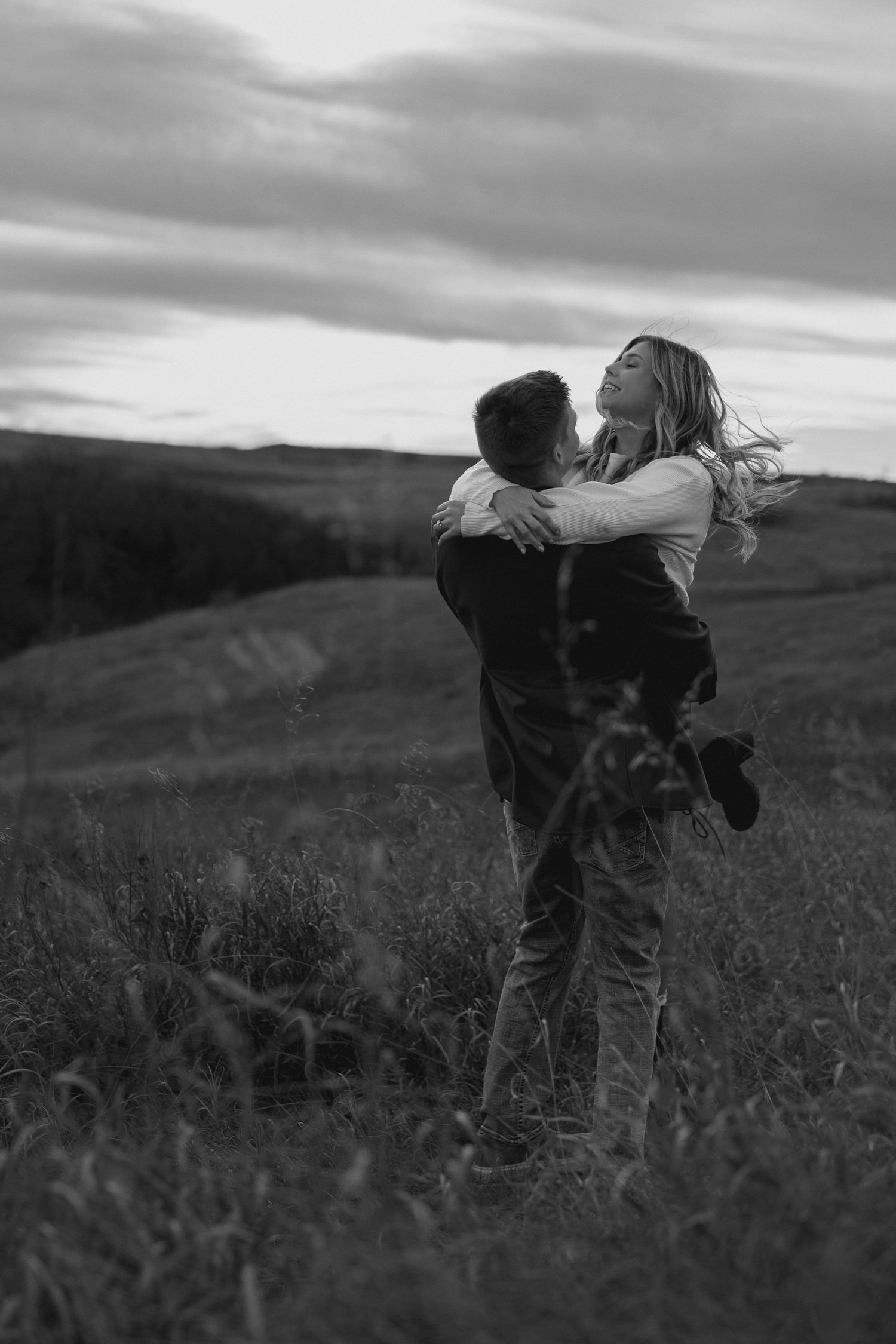 Silhouetted couple sharing an intimate moment in a meadow at dusk.