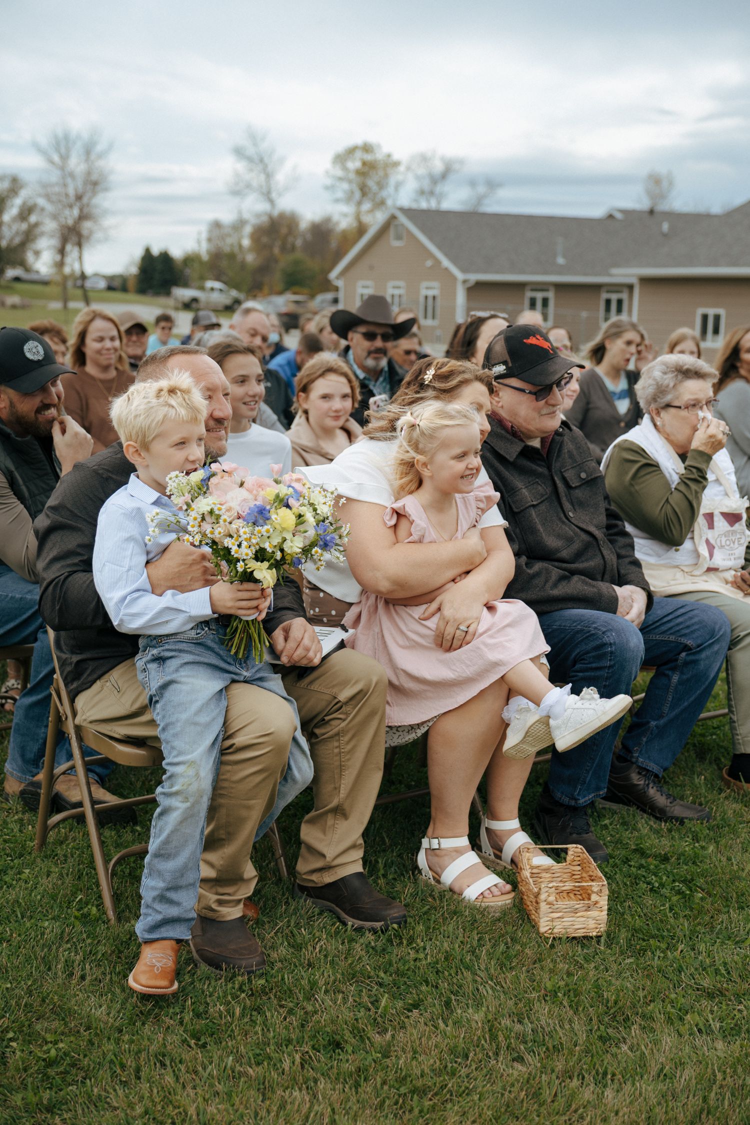 Wedding ceremony guests seated on wooden chairs in an outdoor venue.
