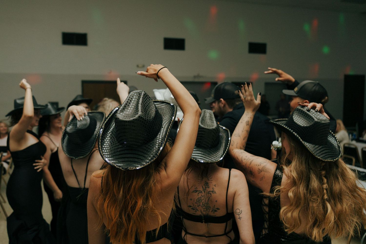 Wedding reception crowd wearing dark hats with hands raised in celebration.