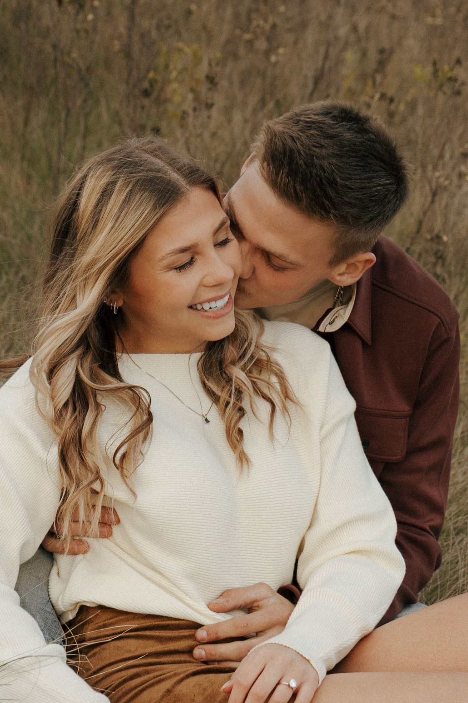 Tender moment between couple lying in tall grass during golden hour.
