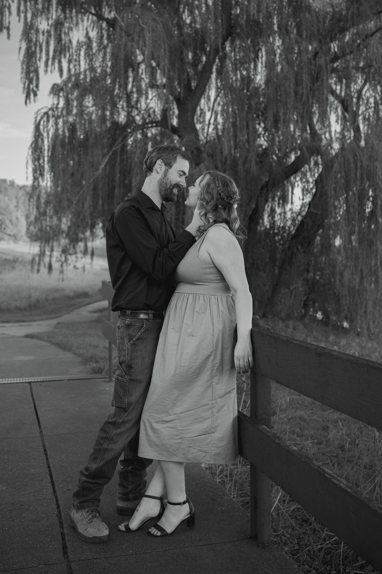 man brushing hair back for fiancee during engagement session with weeping willow in background