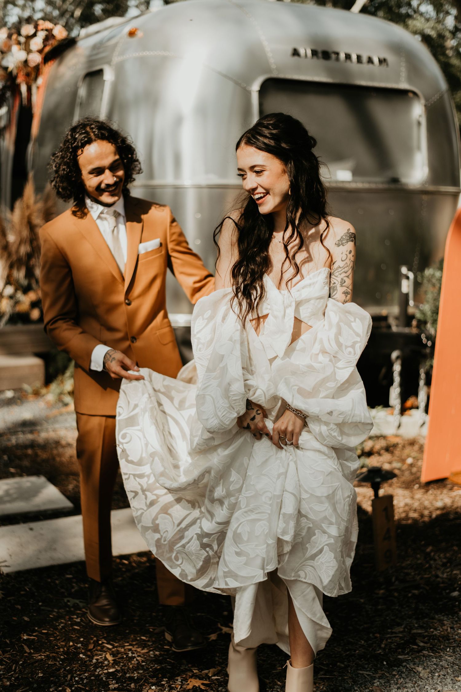 Newlyweds laughing together in front of silver Airstream trailer in Cape Cod.