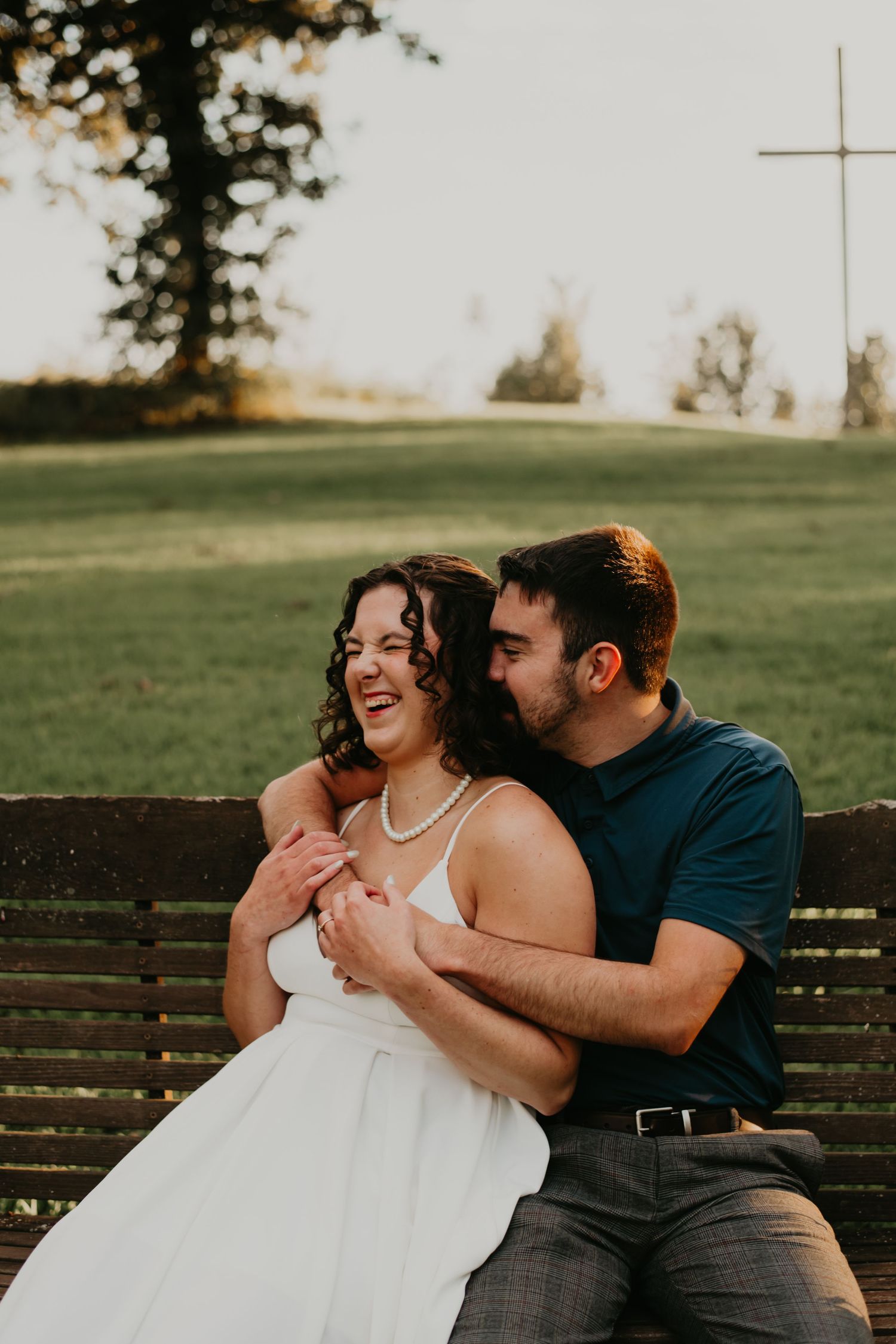 A couple shares a tender moment of laughter and joy while sitting together on a wooden bench at sunset.