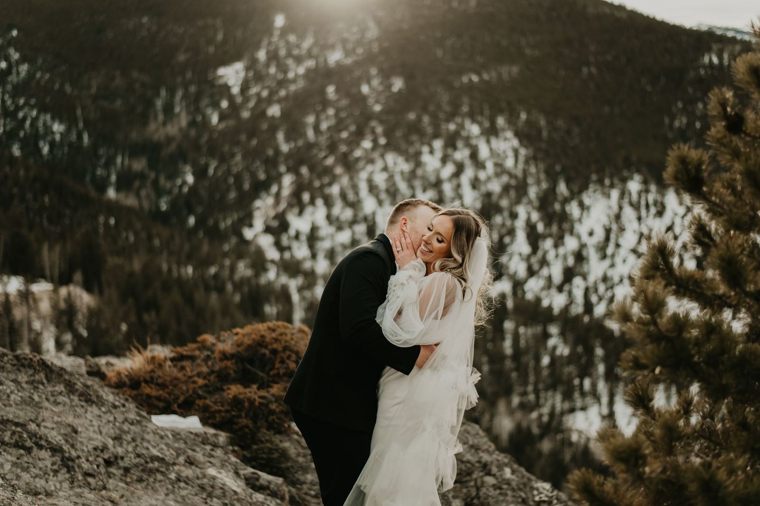 Intimate wedding moment on a mountain cliff overlooking snow-covered peaks in Utah.