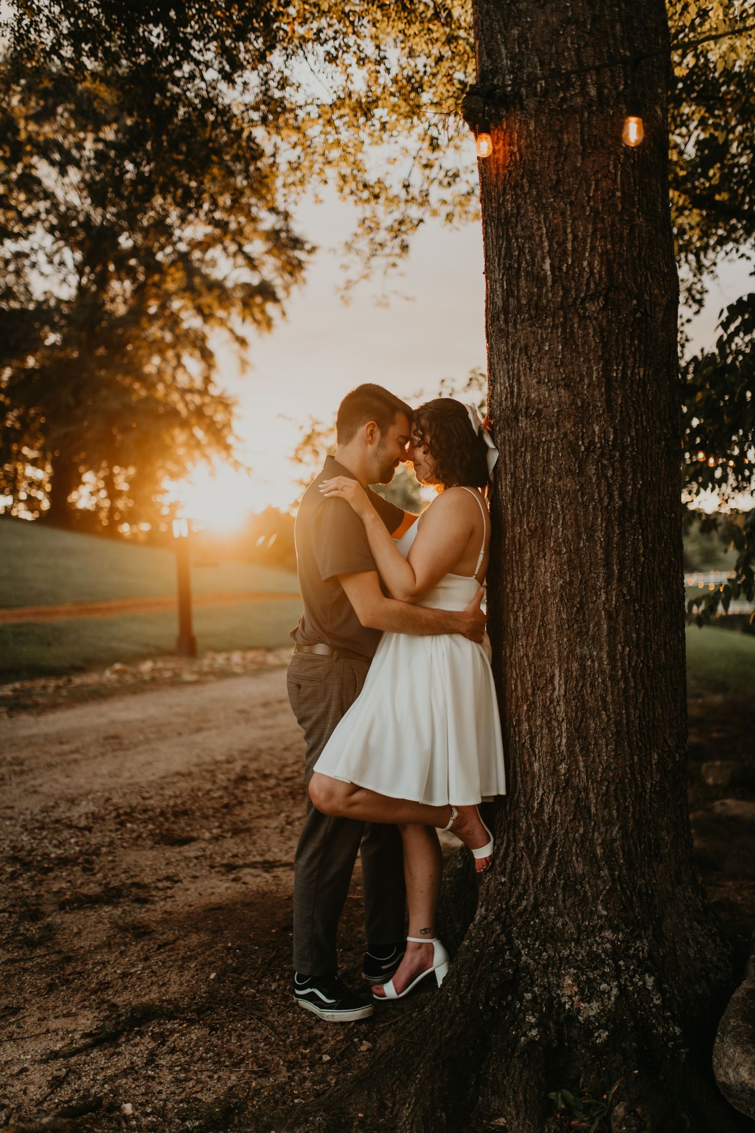 A couple shares a romantic moment against a tree during golden hour sunset in a serene outdoor setting.