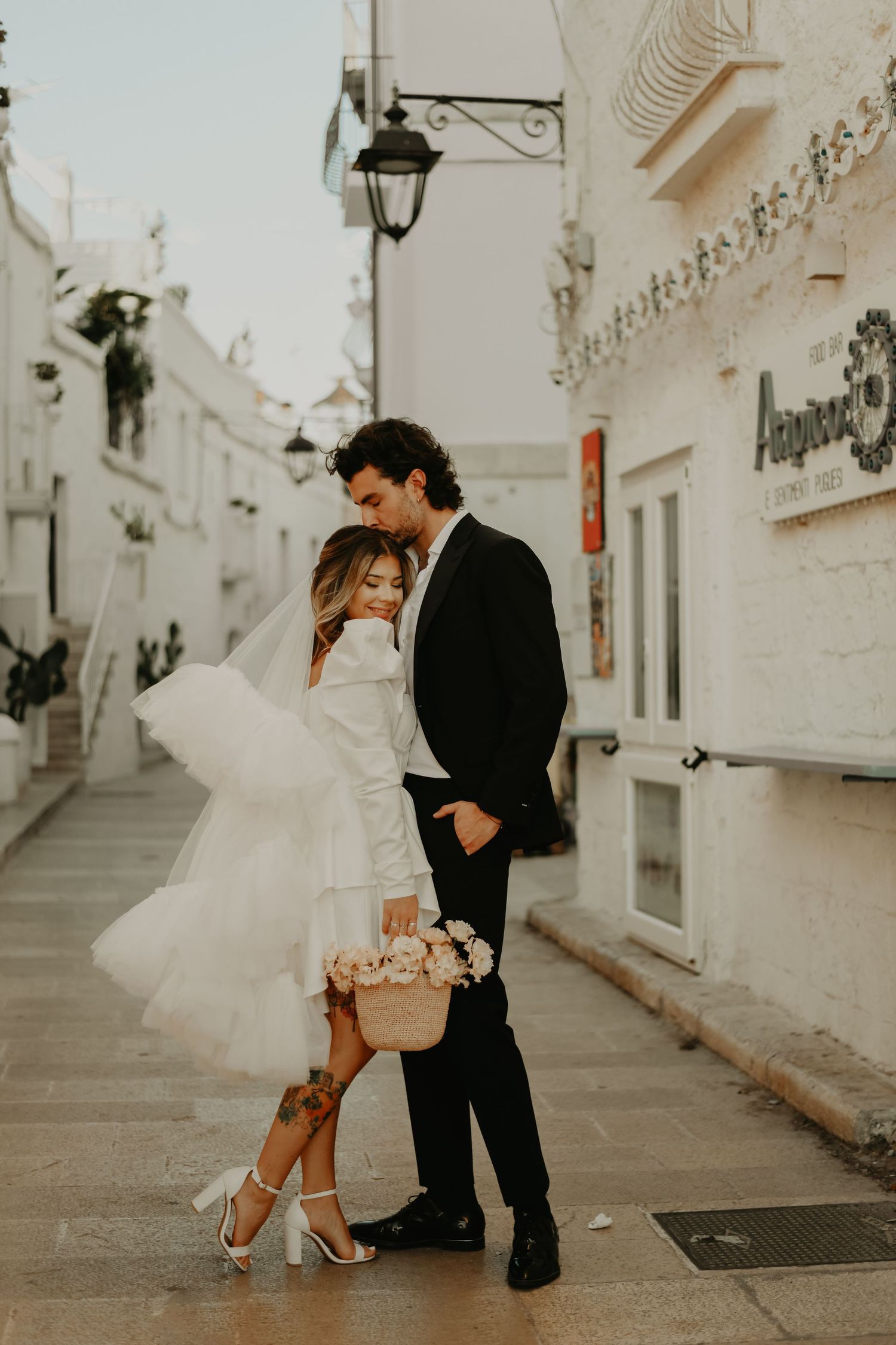 A romantic couple pose on a charming white Mediterranean street with vintage lamp post in Italy.