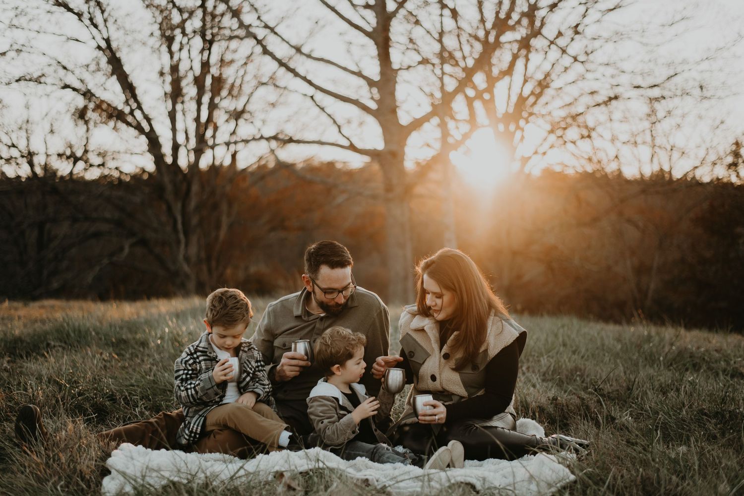 Three people sit together with golden sunlight streaming through autumn trees behind them during an outdoor photo session.