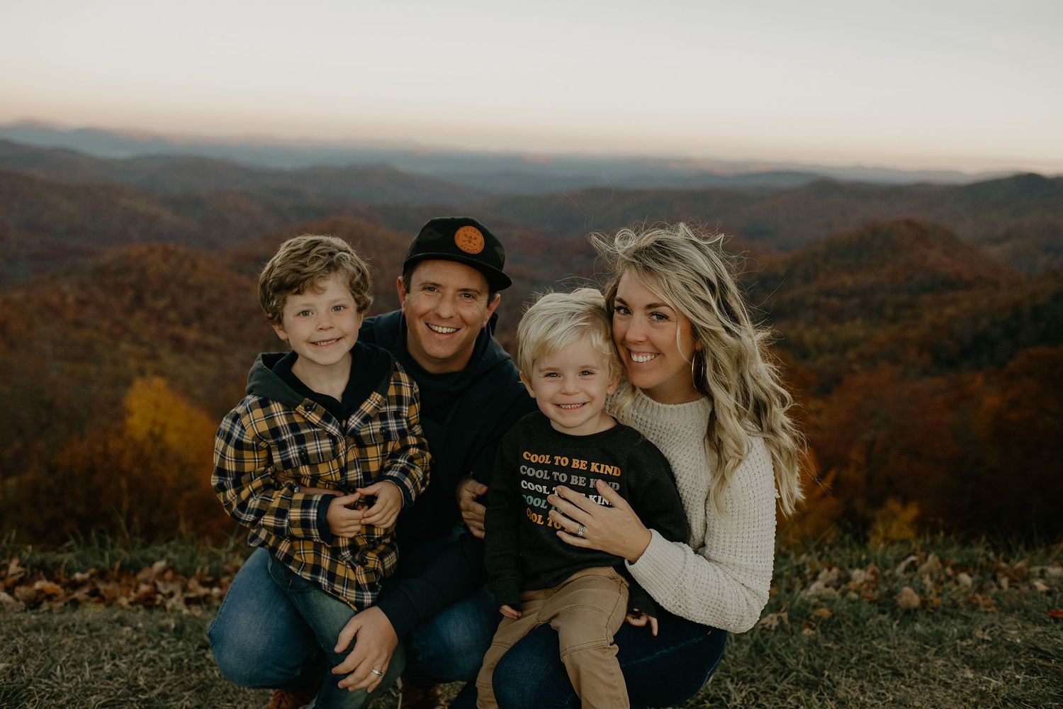 A family sits together enjoying an autumn mountain vista with colorful foliage in the background.