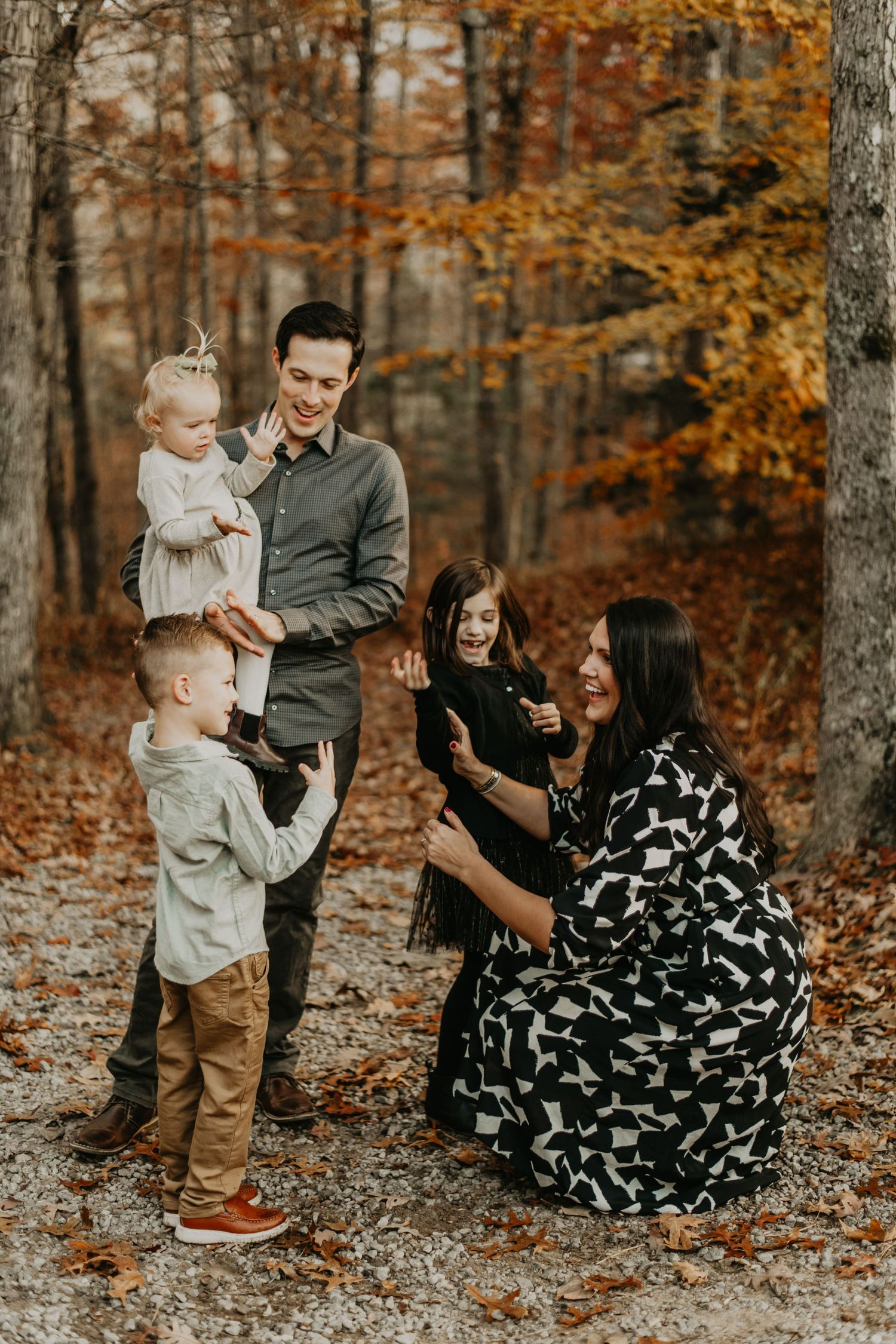 Family enjoying an autumn photoshoot together in a forest with golden fall foliage and leaves on the ground.