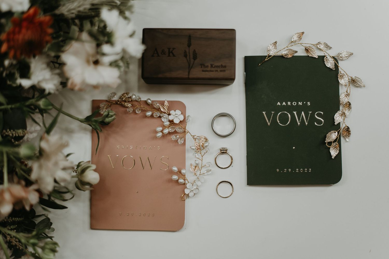 Wedding vows book and wedding rings styled with delicate flowers and greenery on a neutral background.