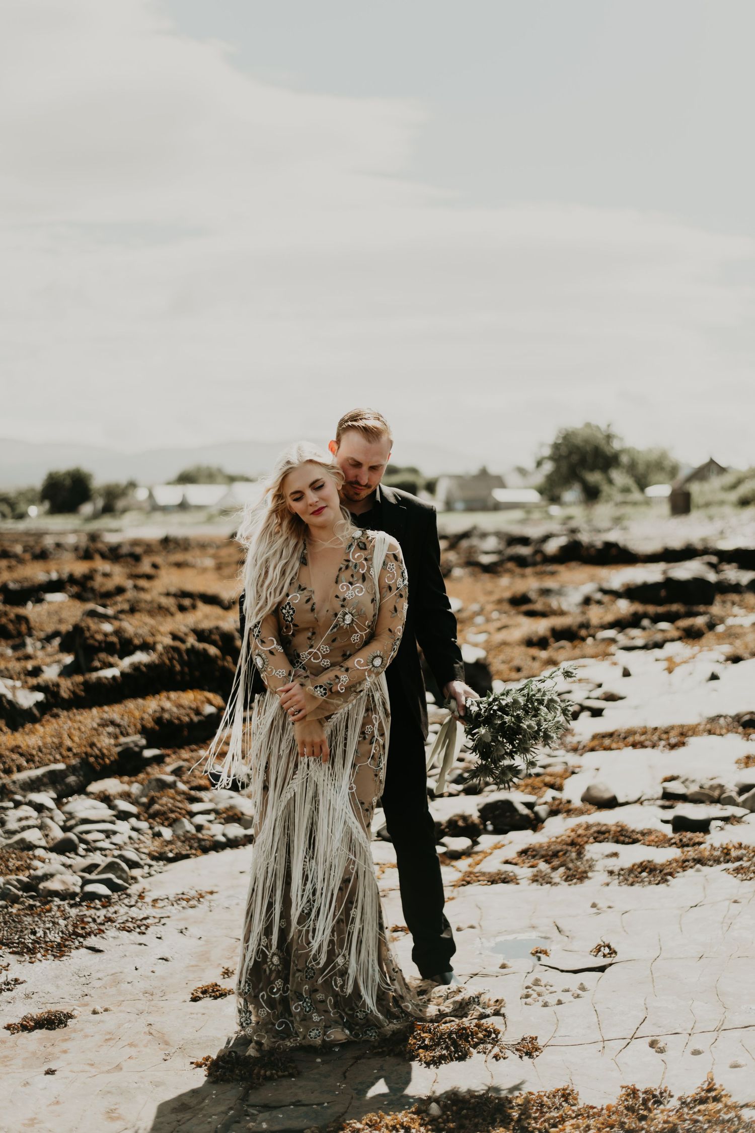 Couple in formal wear embracing on rocky terrain during overcast day in Isle of Skye Scotland.