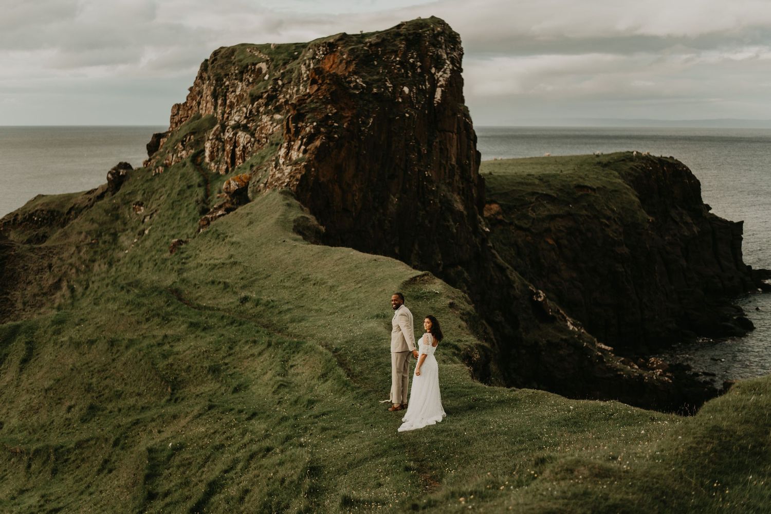 Dramatic cliffside coastal wedding portraits with couple silhouetted against rugged ocean landscape in Isle of Skye Scotland.