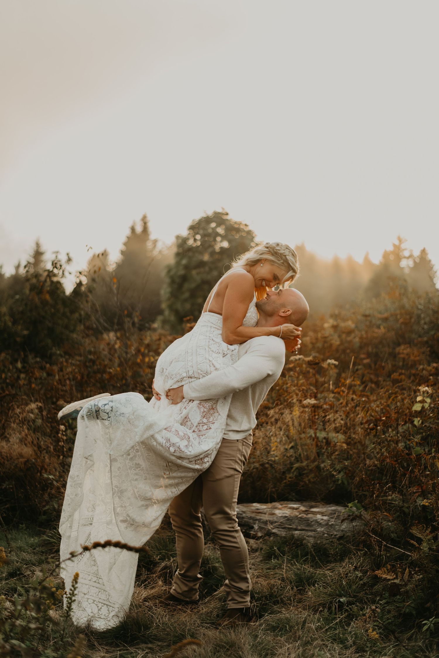 Couple in wedding attire embracing in golden sunset light on mountaintop in Asheville north Carolina.