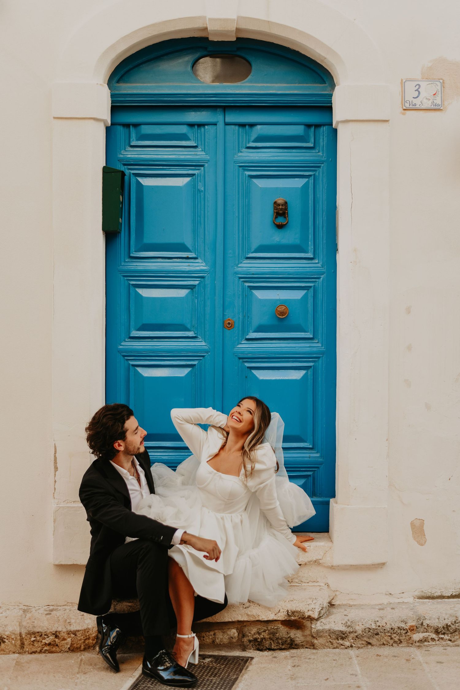A couple shares a playful moment in front of a bright blue vintage door in Italy.