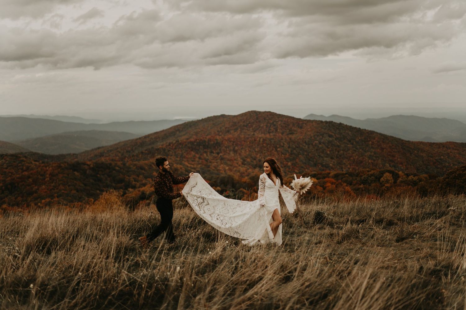 Rolling mountains and moody skies frame ethereal bridal portraits in golden field in North Carolina.