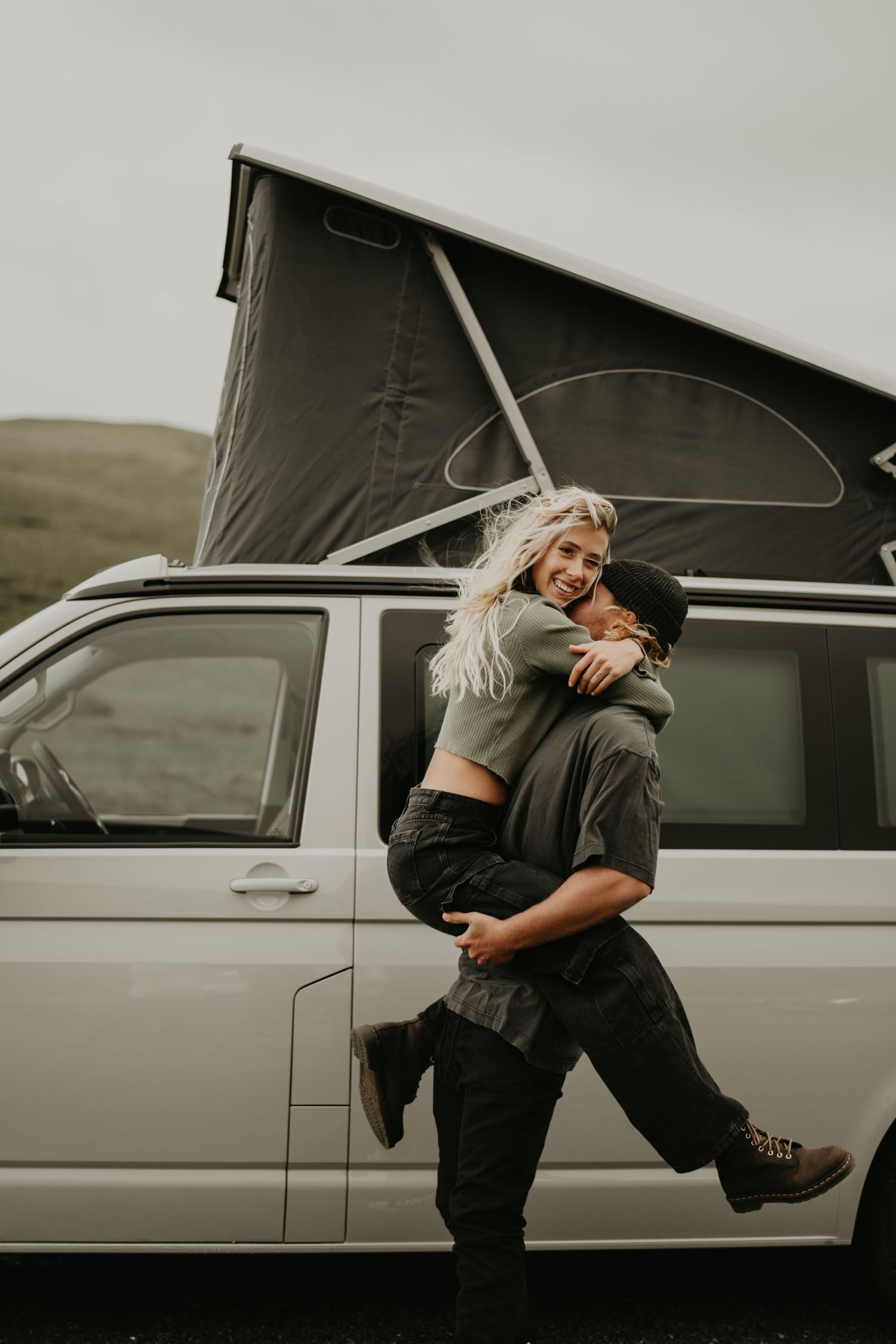Two people hugging beside a white van in a minimalist monochrome outdoor setting.