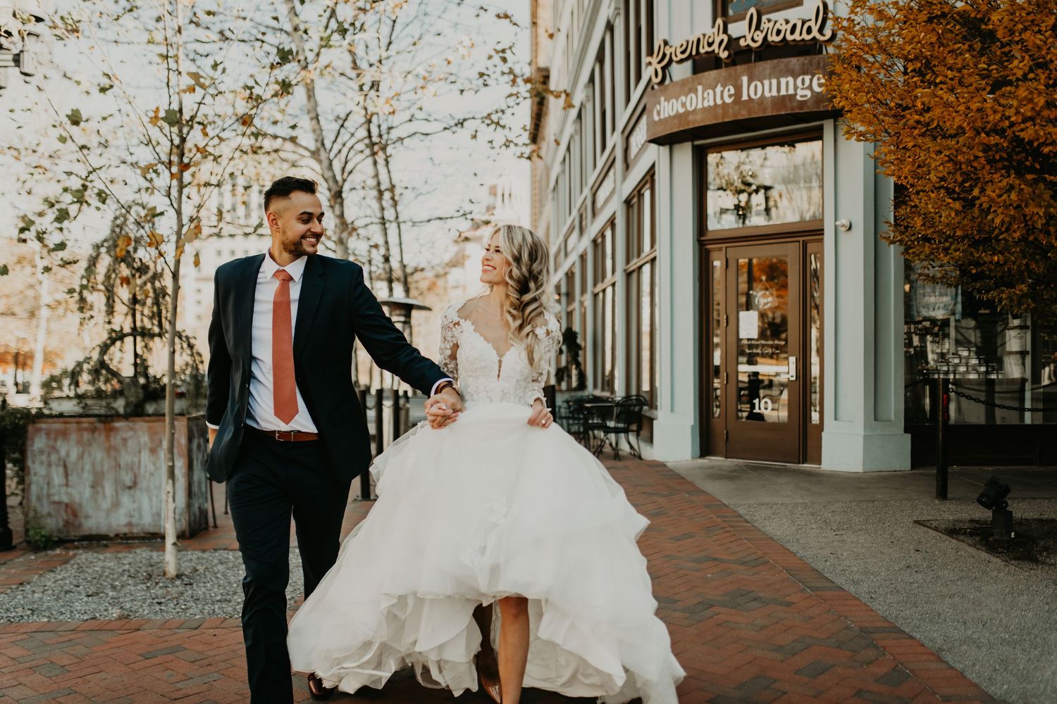 Joyful couple running along brick sidewalk in urban setting during autumn in Asheville north Carolina.