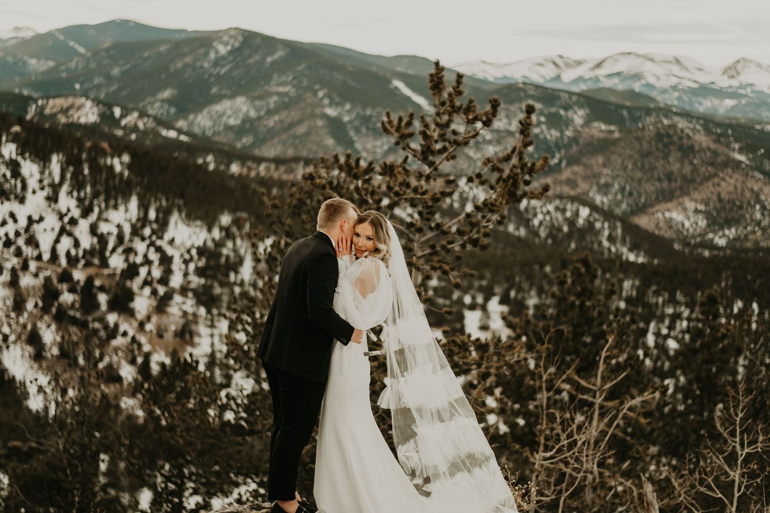Winter wedding couple against snowy mountain backdrop in golden light in Utah.