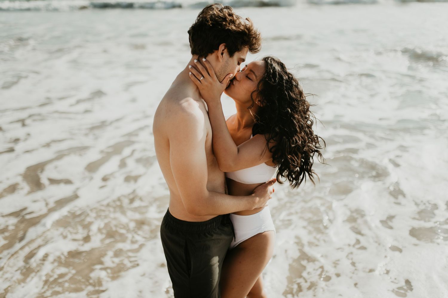 A romantic couple embraces on a sandy beach during sunset, creating an intimate silhouette against the ocean backdrop.
