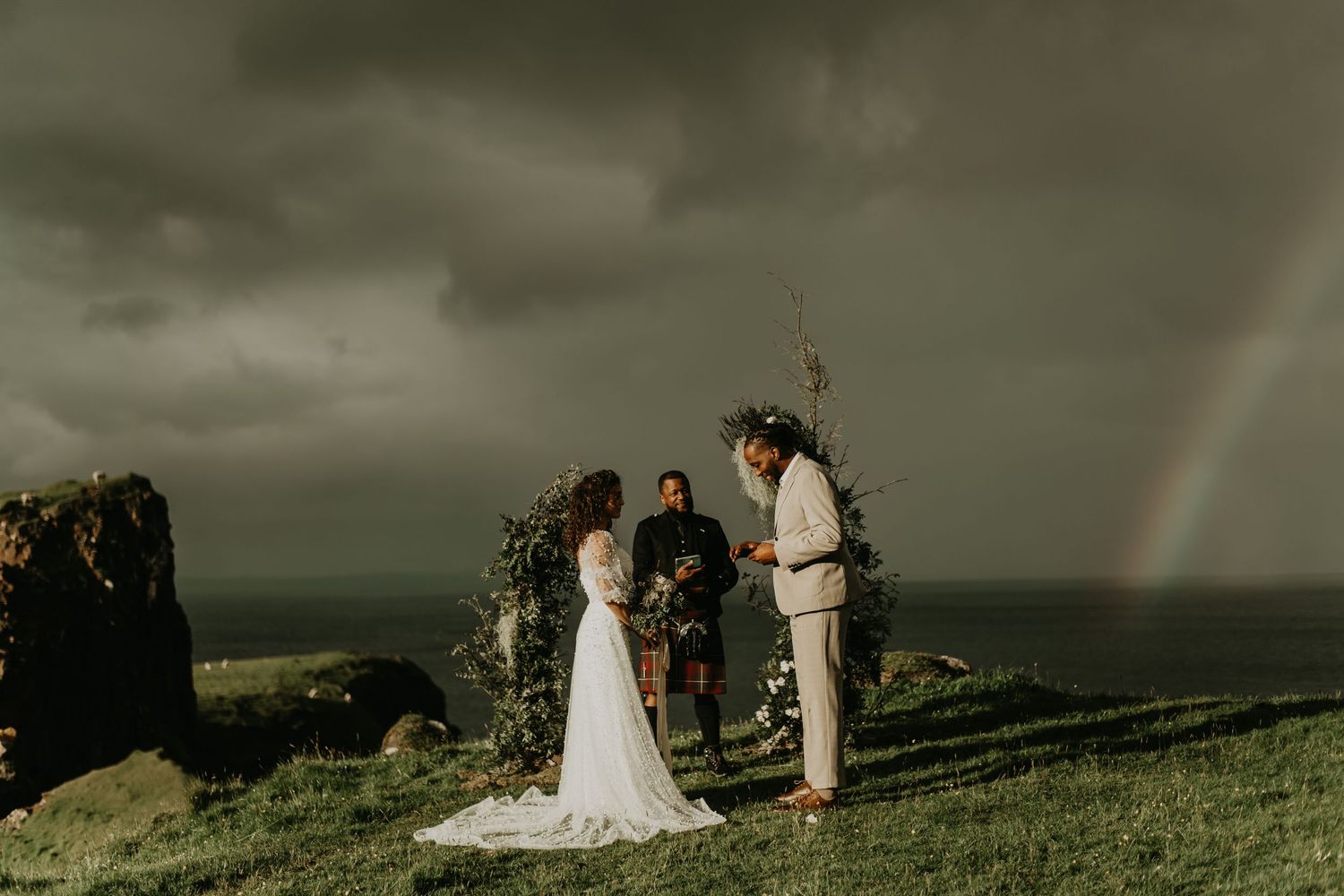 Coastal wedding ceremony with dramatic stormy sky and rainbow in backdrop in isle of Skye Scotland.