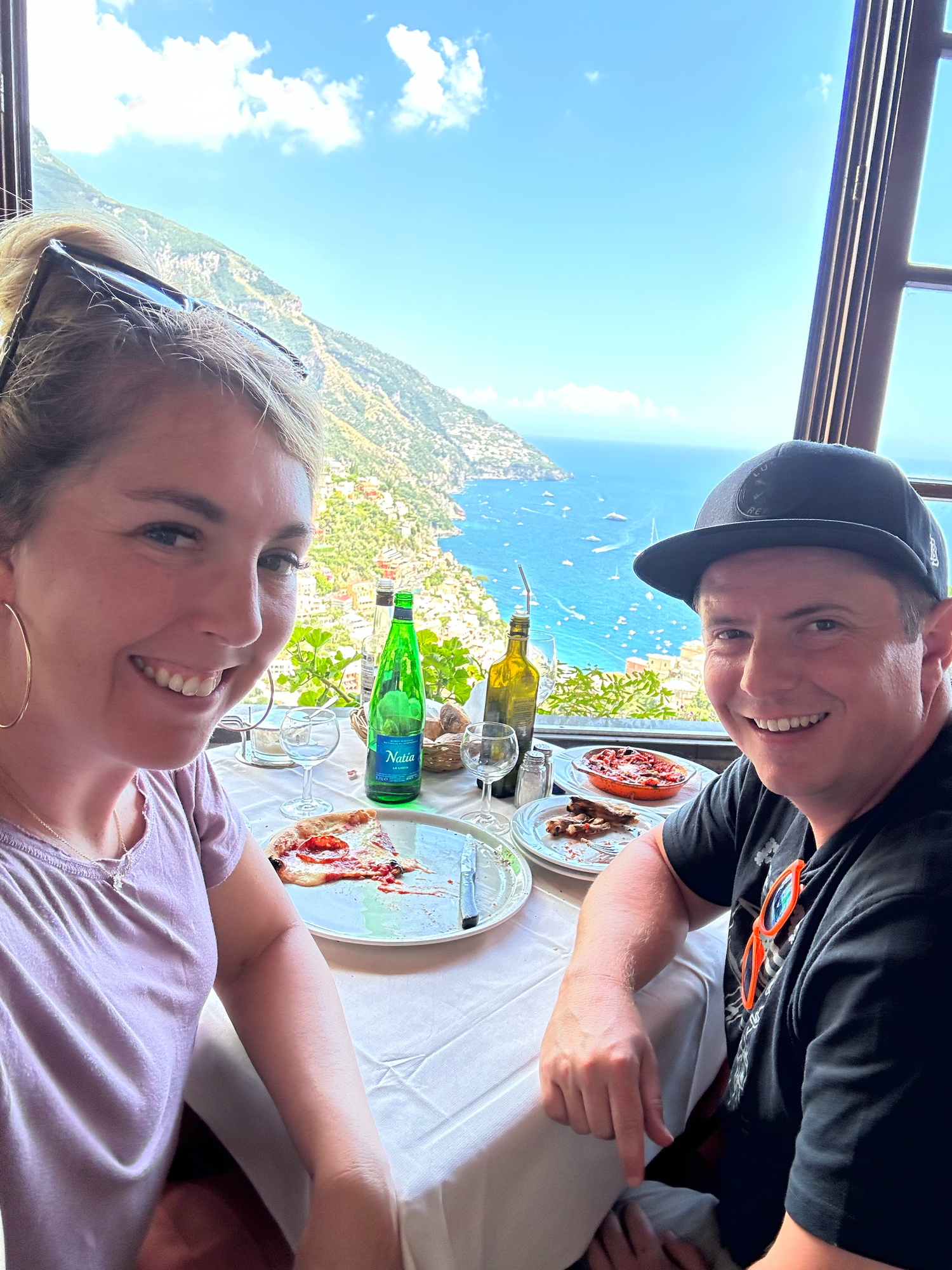 Couple dining at restaurant with stunning coastal view of Mediterranean cliffs.