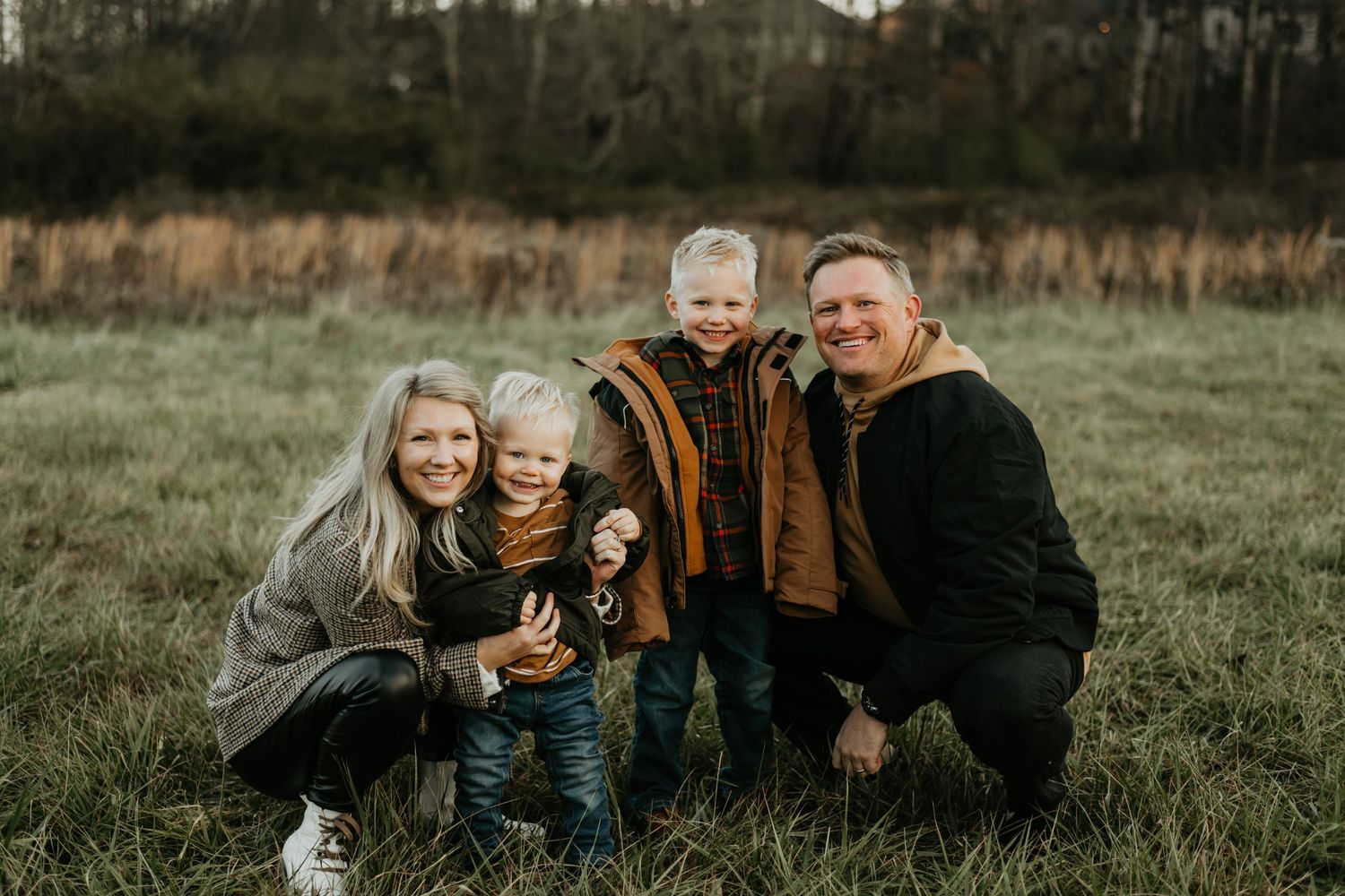 A family group poses together in a grassy field on an overcast autumn day.