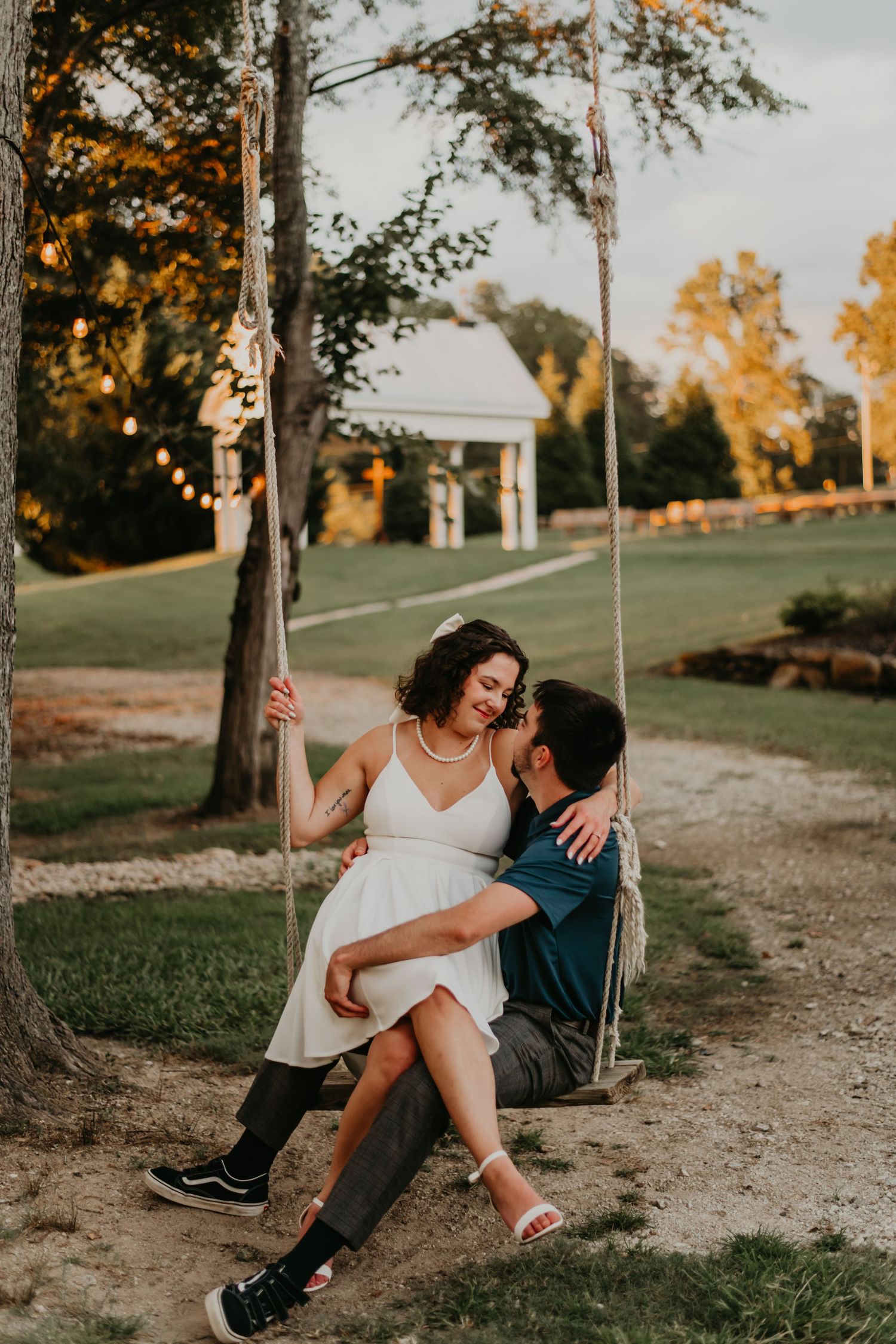 Couple enjoying a romantic sunset moment together while sitting on a rustic wooden swing in an outdoor setting.