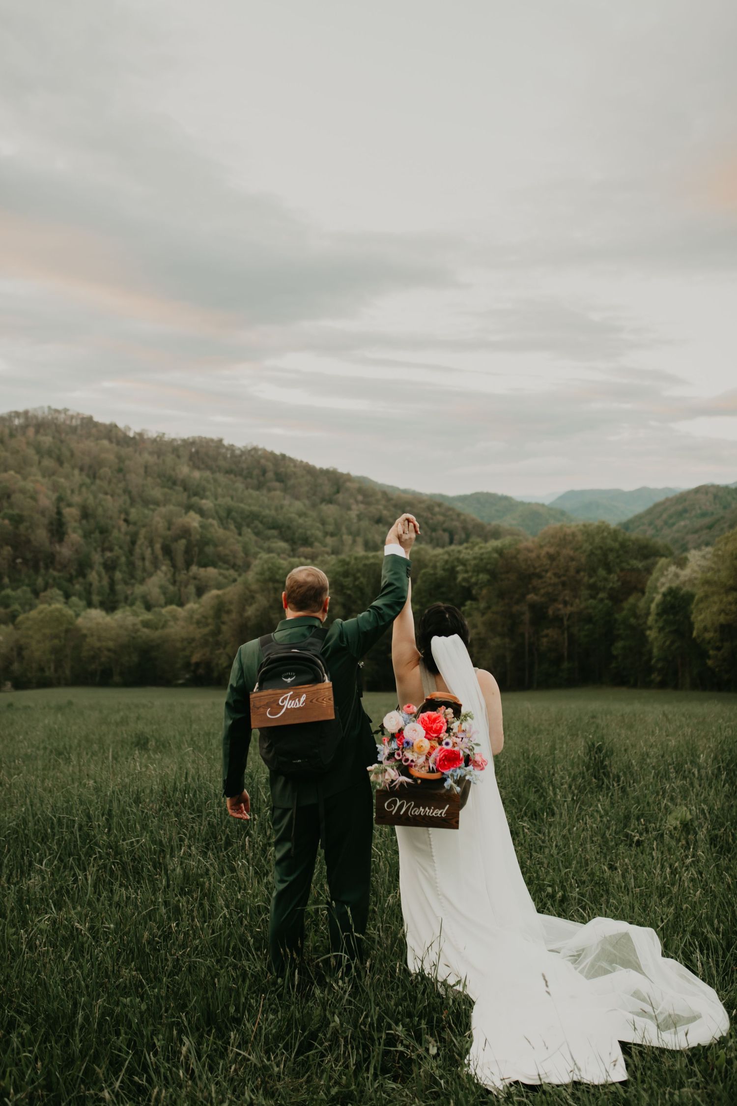 Couple in wedding attire celebrating with raised hands in mountain meadow in North Carolina.
