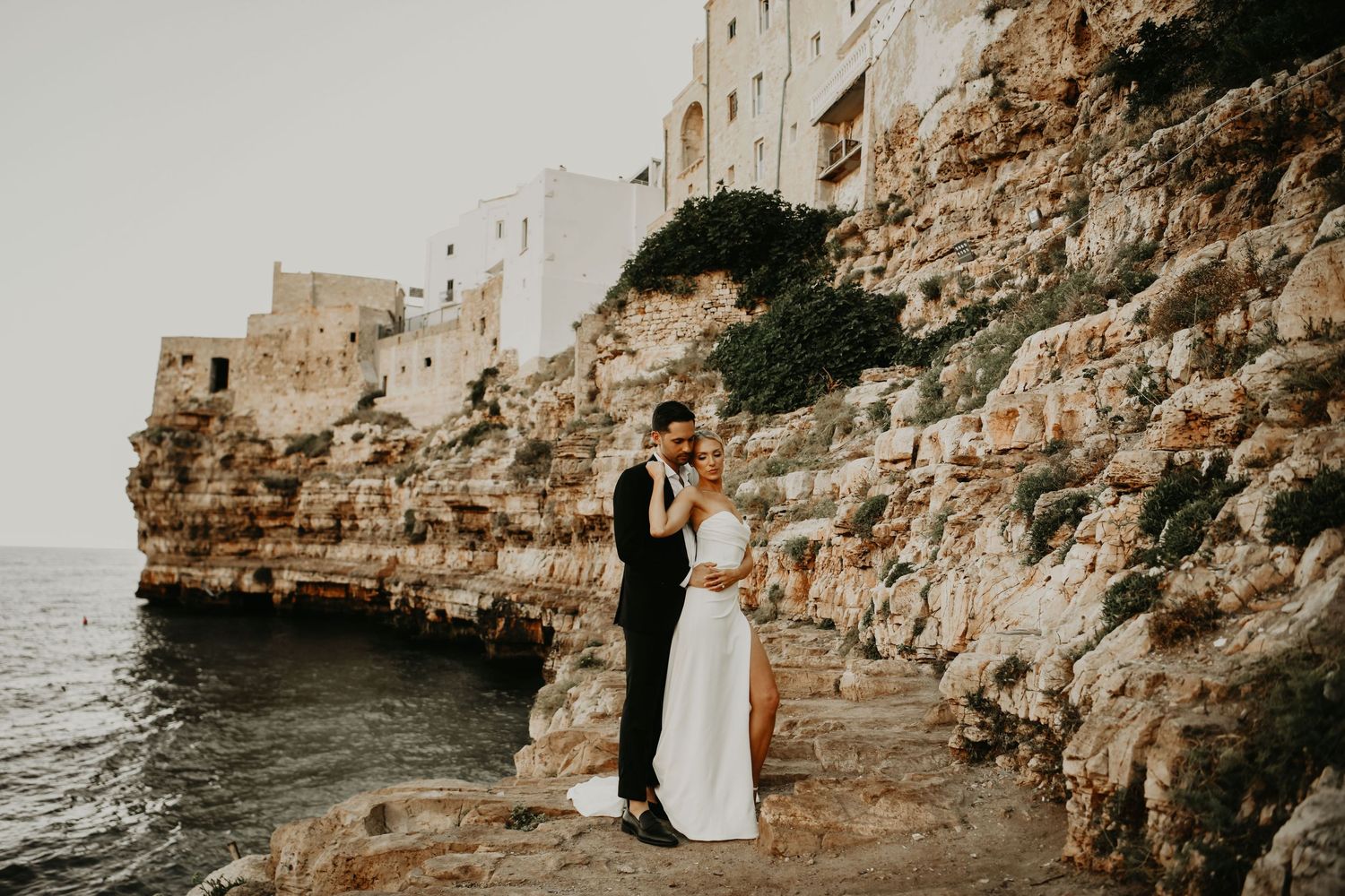 A couple in wedding attire stands on dramatic coastal cliffs overlooking the Mediterranean Sea in Puglia Italy.
