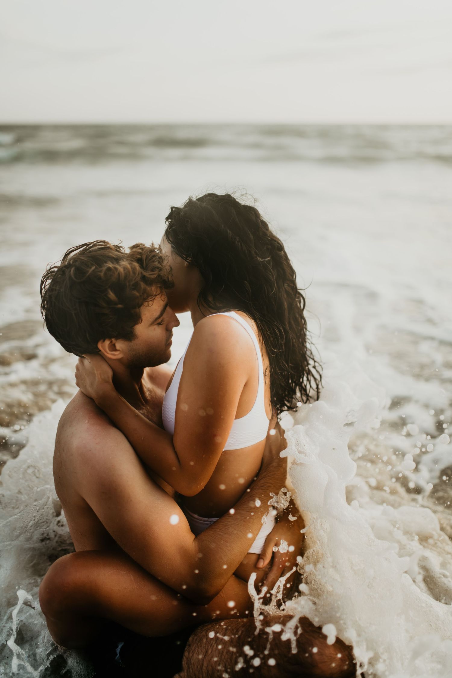 Romantic couple embracing in ocean waves during sunset photoshoot.