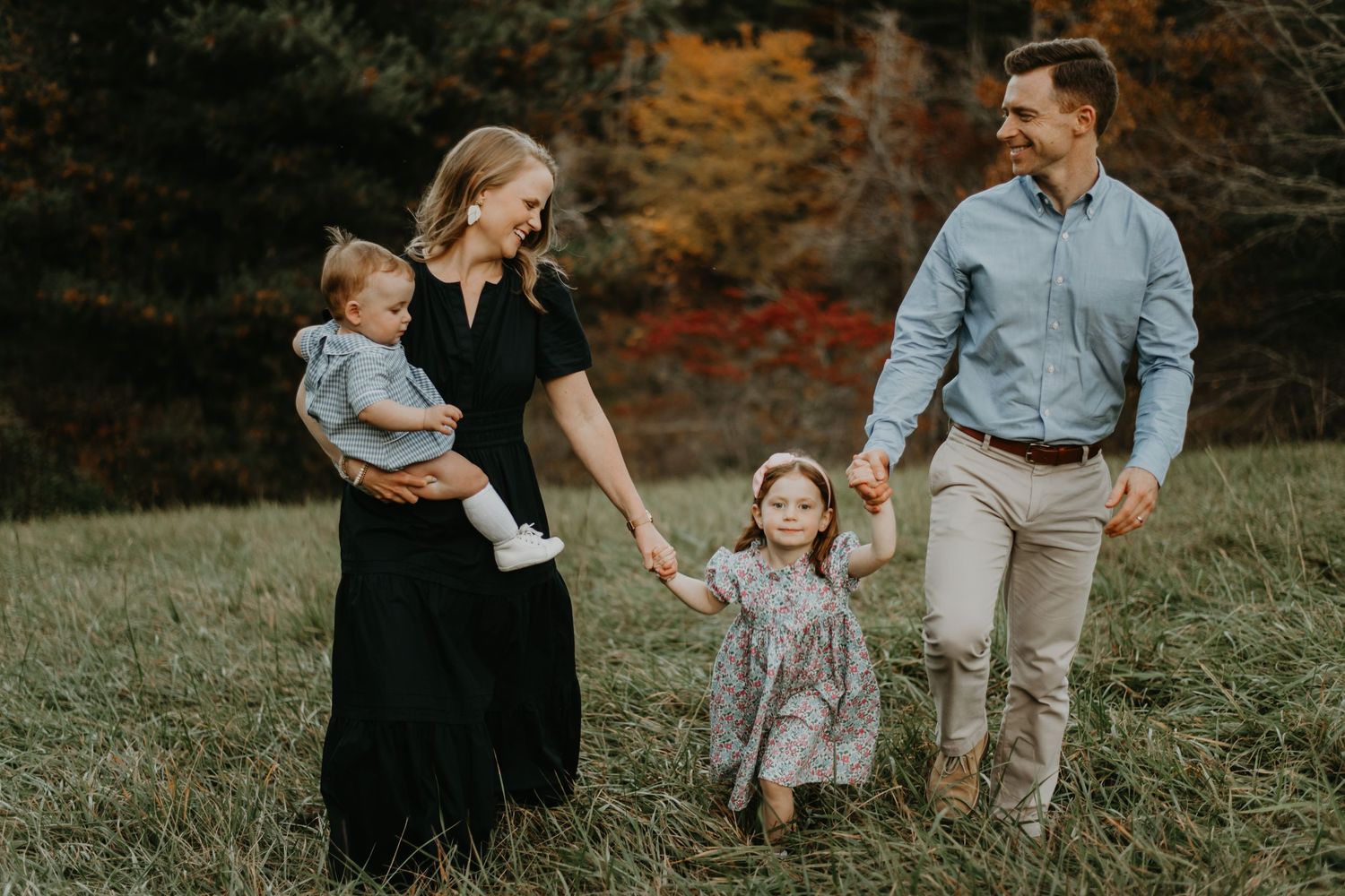 Fall family photoshoot with parents and children walking through a golden autumn field at sunset.
